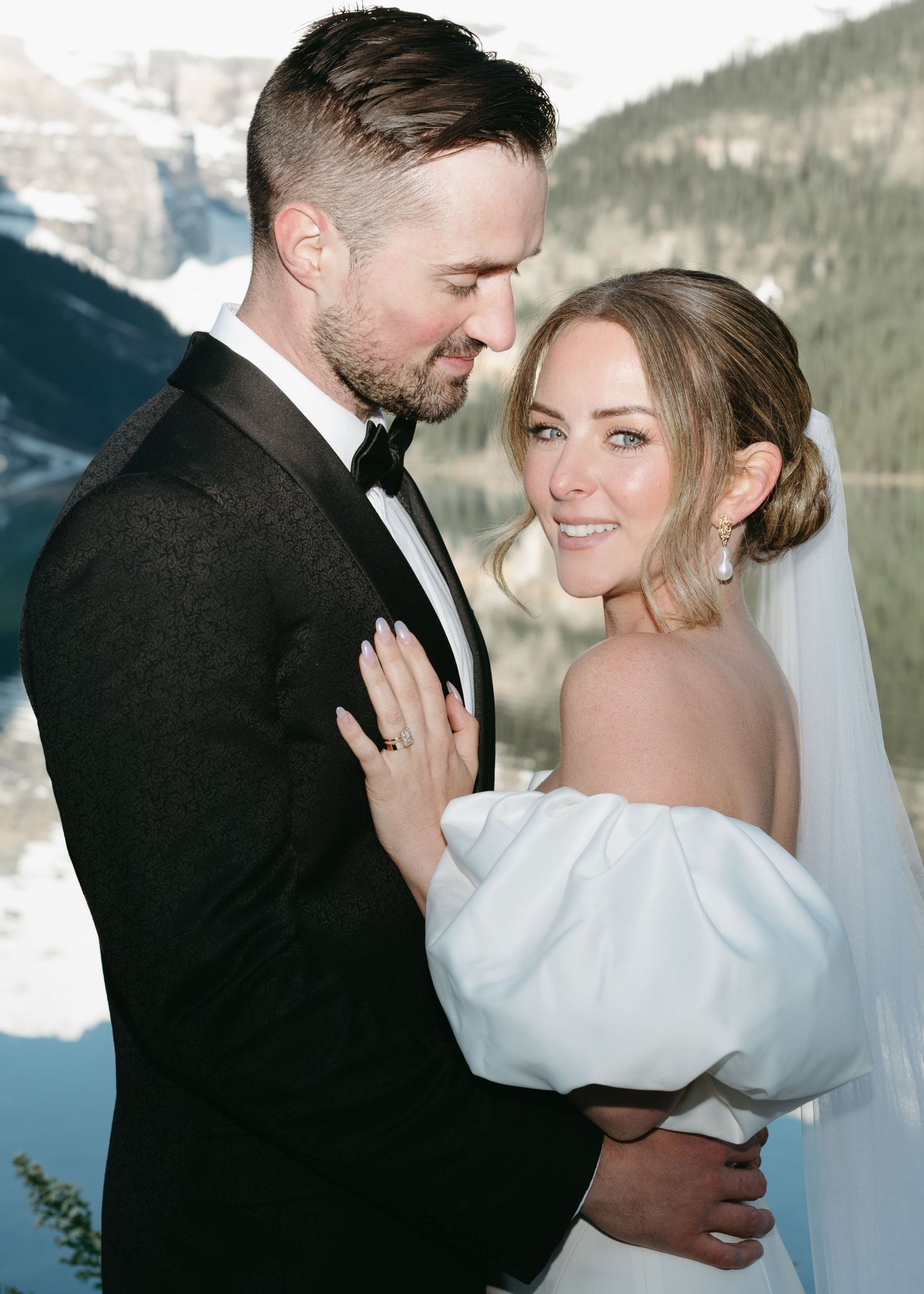 A romantic winter wedding portrait shows a couple embracing in front of snow-capped mountains.