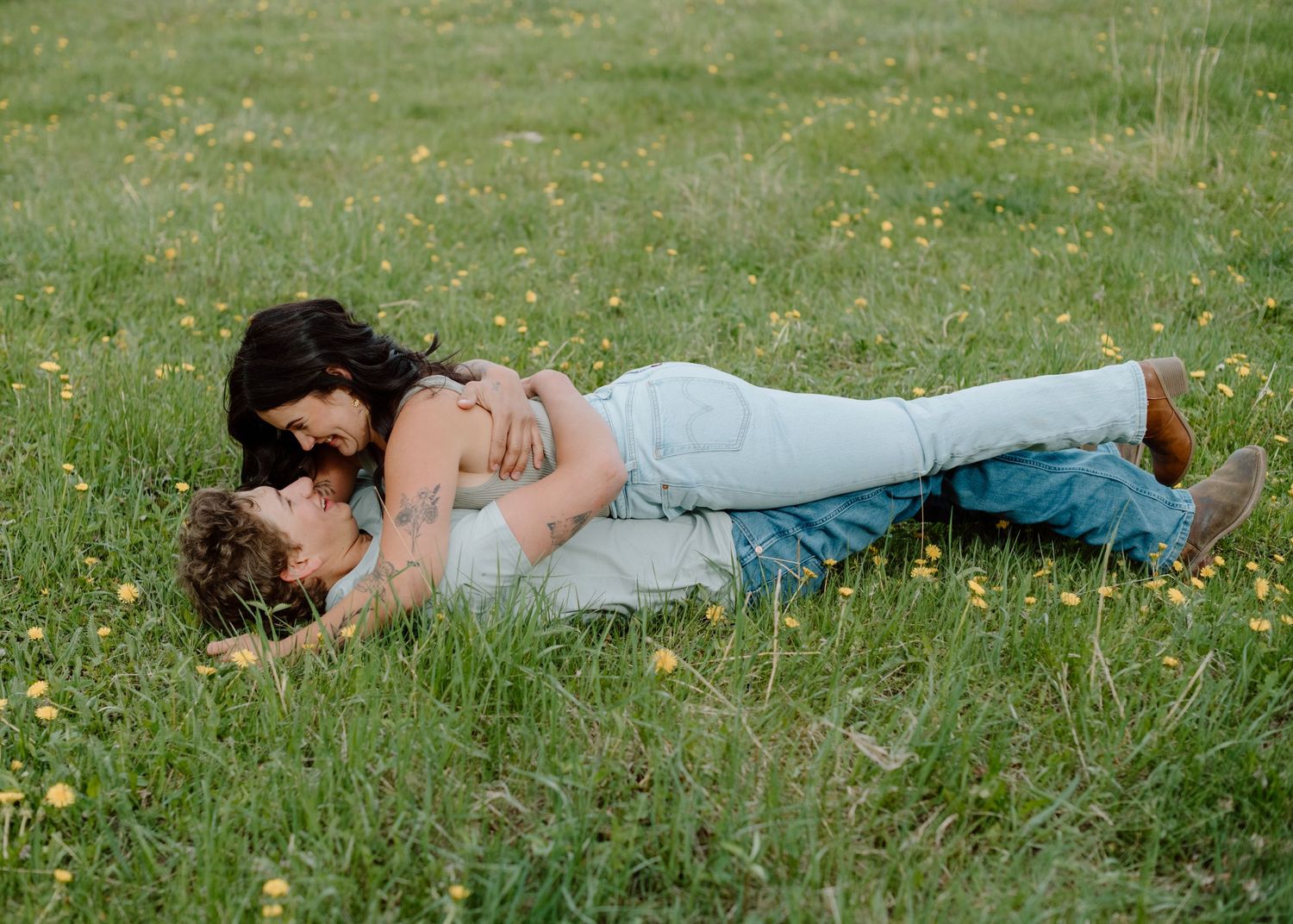 Two people lying down together in a field of wildflowers and grass. Calgary Alberta Engagement Photographer.