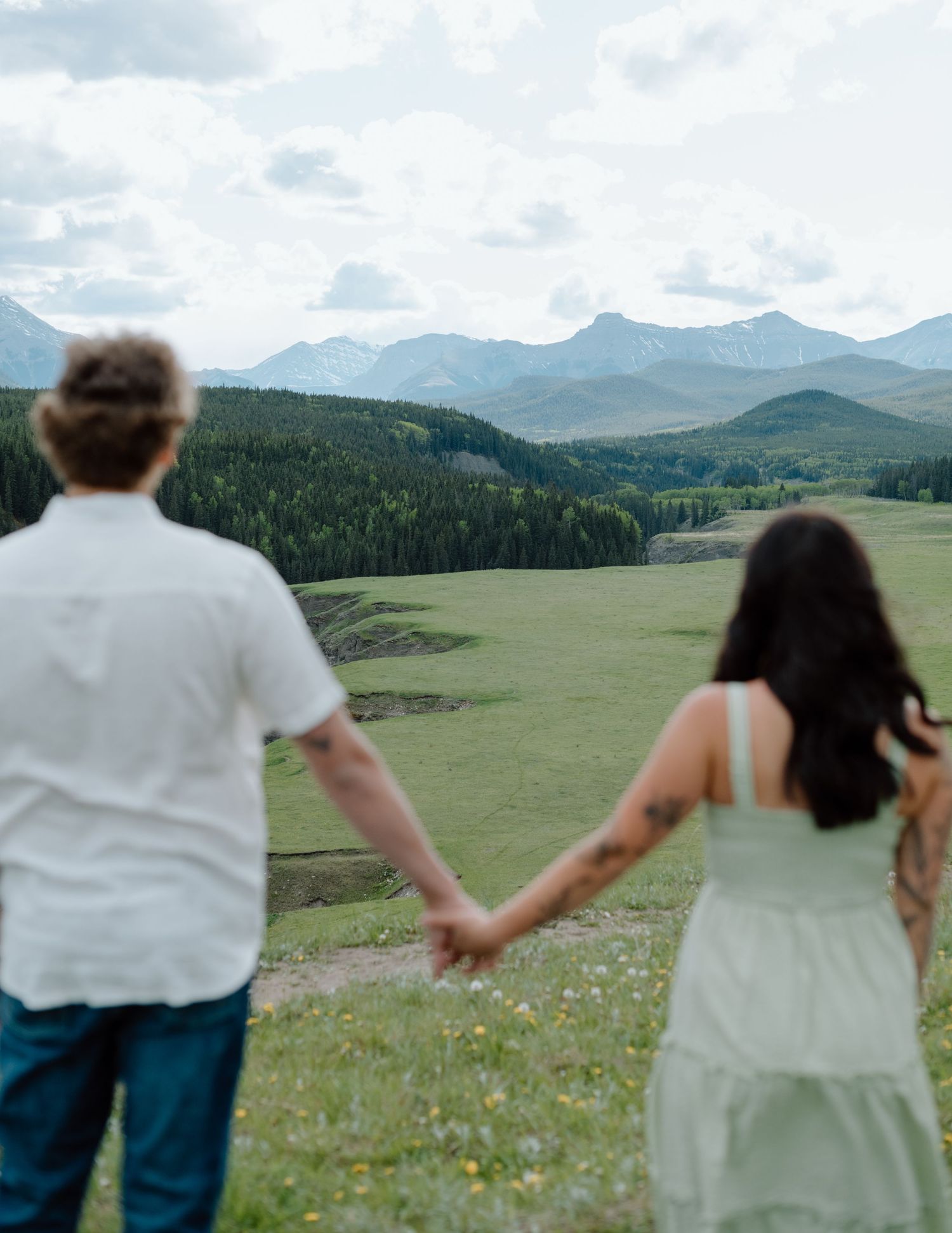 Two people holding hands while overlooking a dramatic mountain valley landscape in Calgary, Alberta Calgary Lifestyle and Engagement Photo