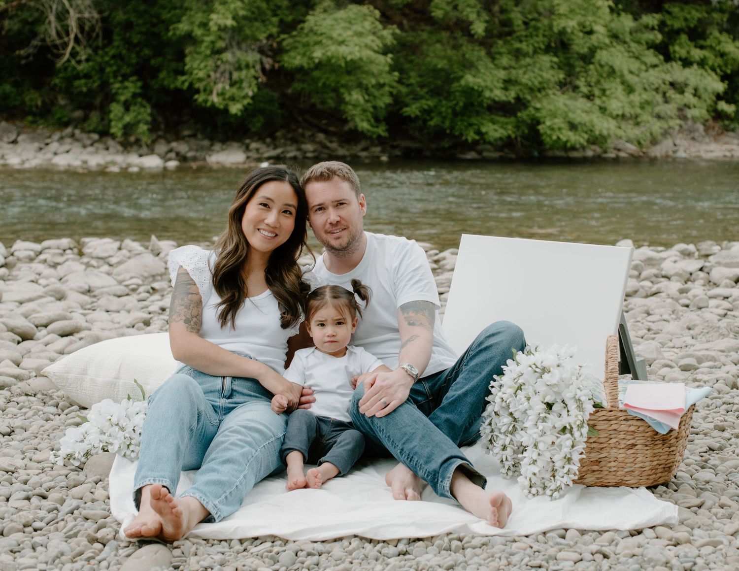 A family lying together on a white blanket outdoors enjoying quality time in nature. Calgary Alberta Family and Maternity Photographer.
