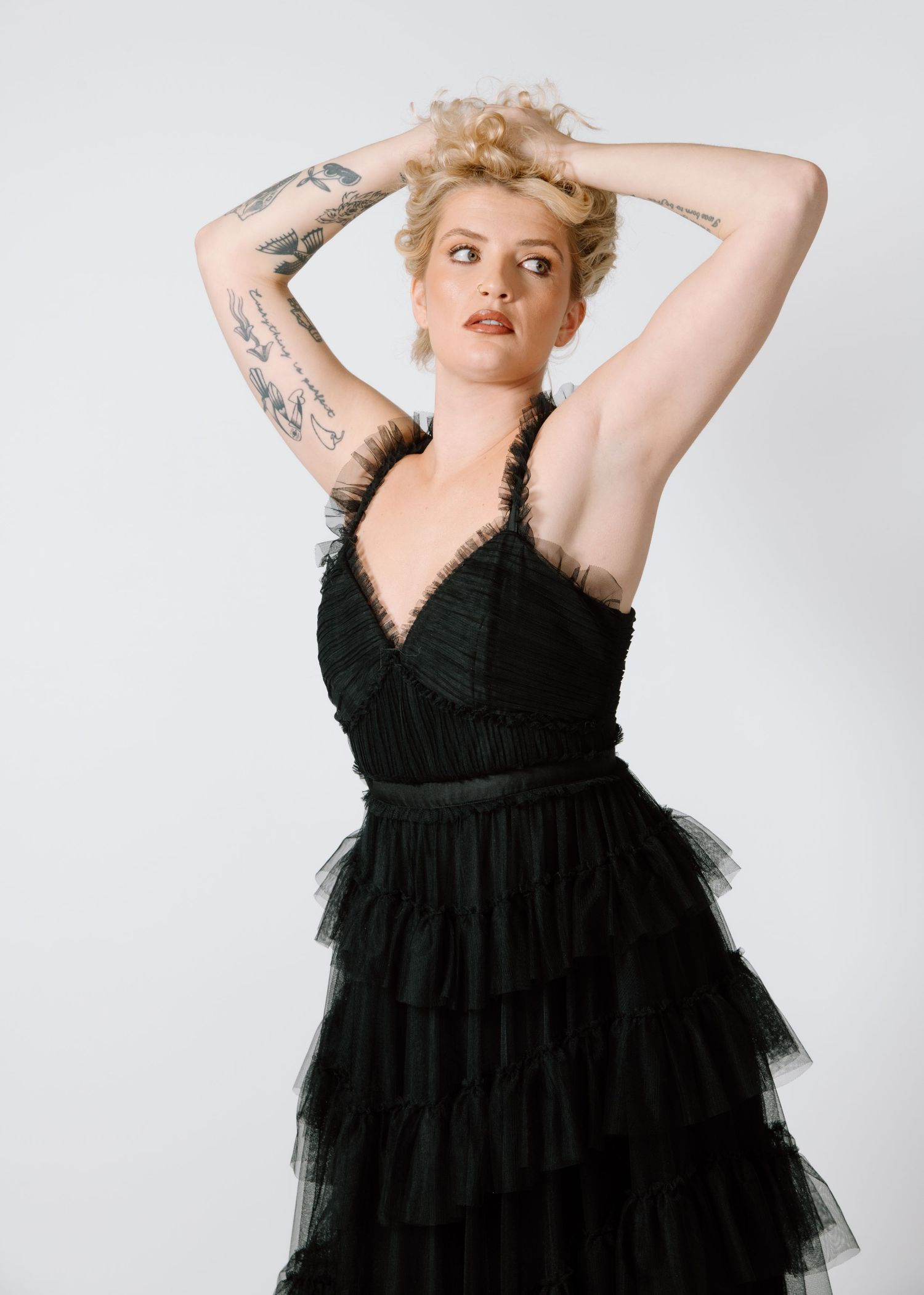 Model in black tulle dress with tattoos poses dramatically against white backdrop. Calgary Alberta Branding Photographer.
