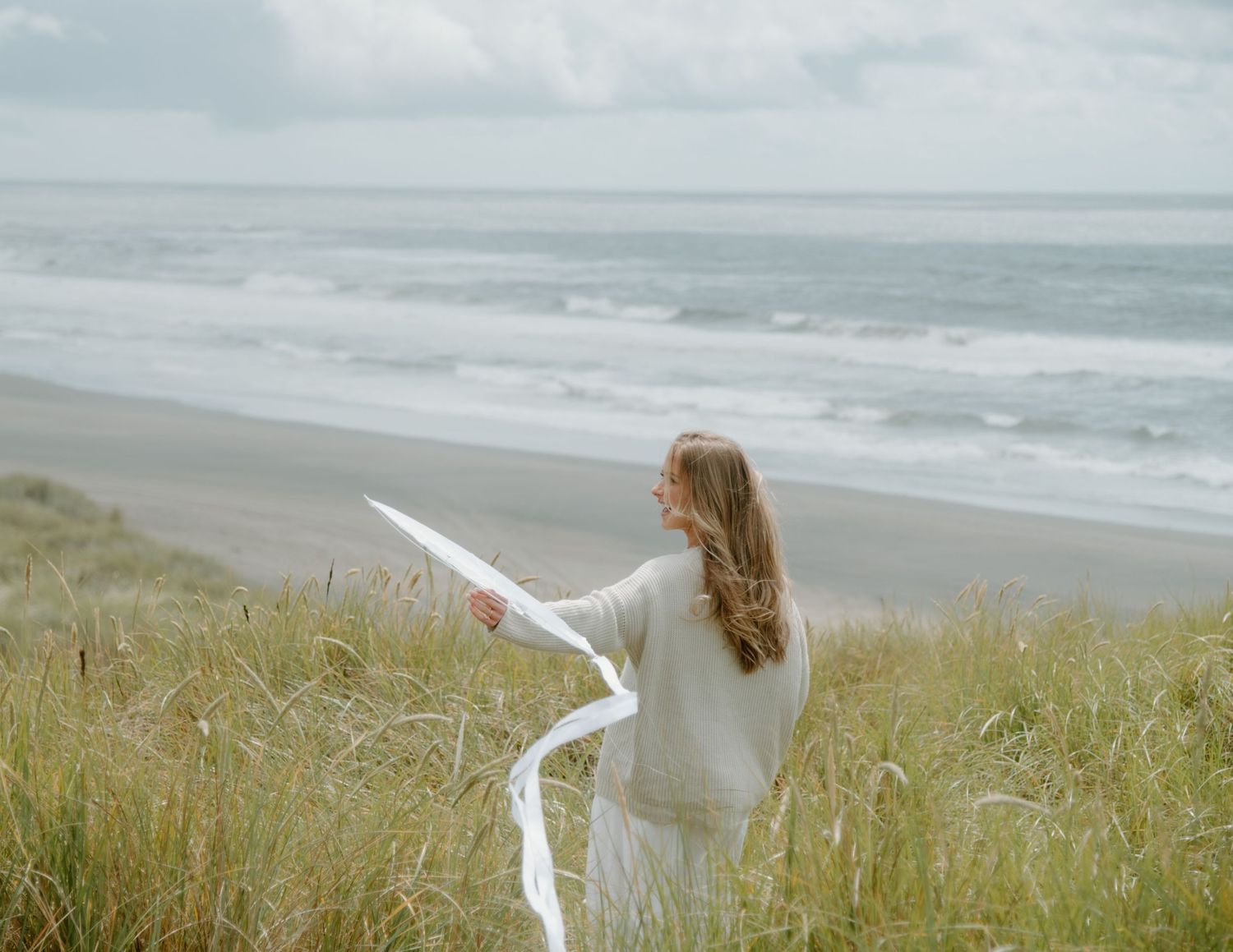 A figure holds flowing white fabric on a scenic coastal overlook on Oregon Coast. Calgary Lifestyle and Engagement Photographer.