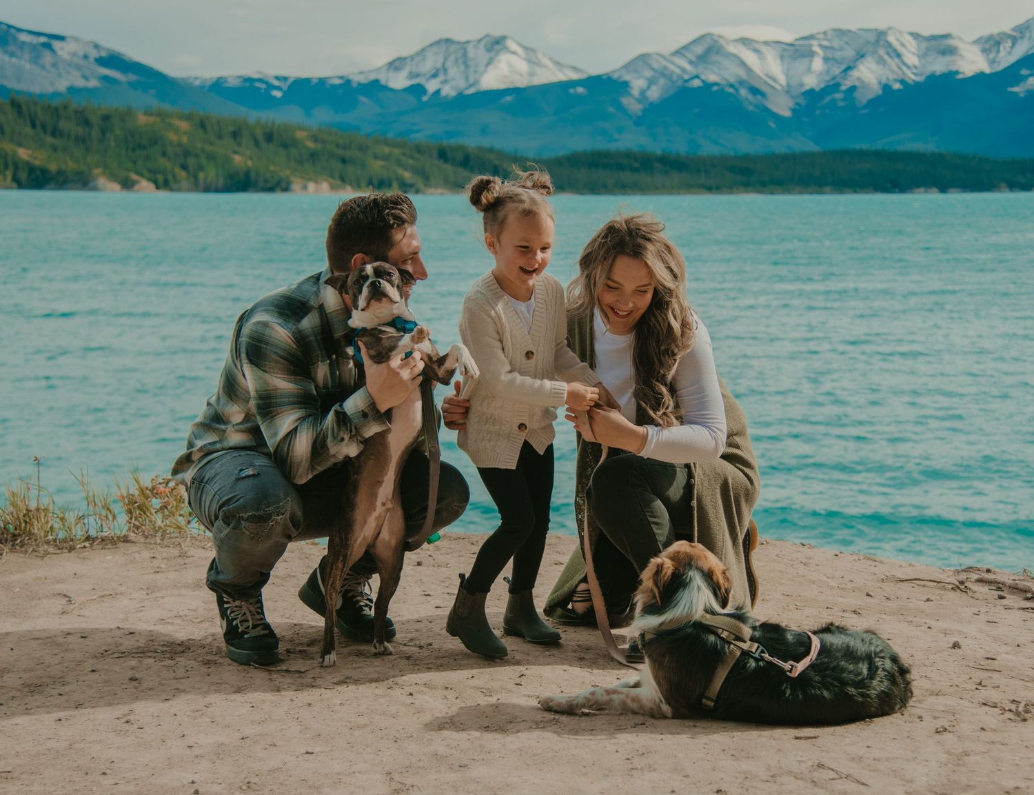 Wedding party sits casually on a beach with mountain and lake views. Calgary Family and Maternity Photographer