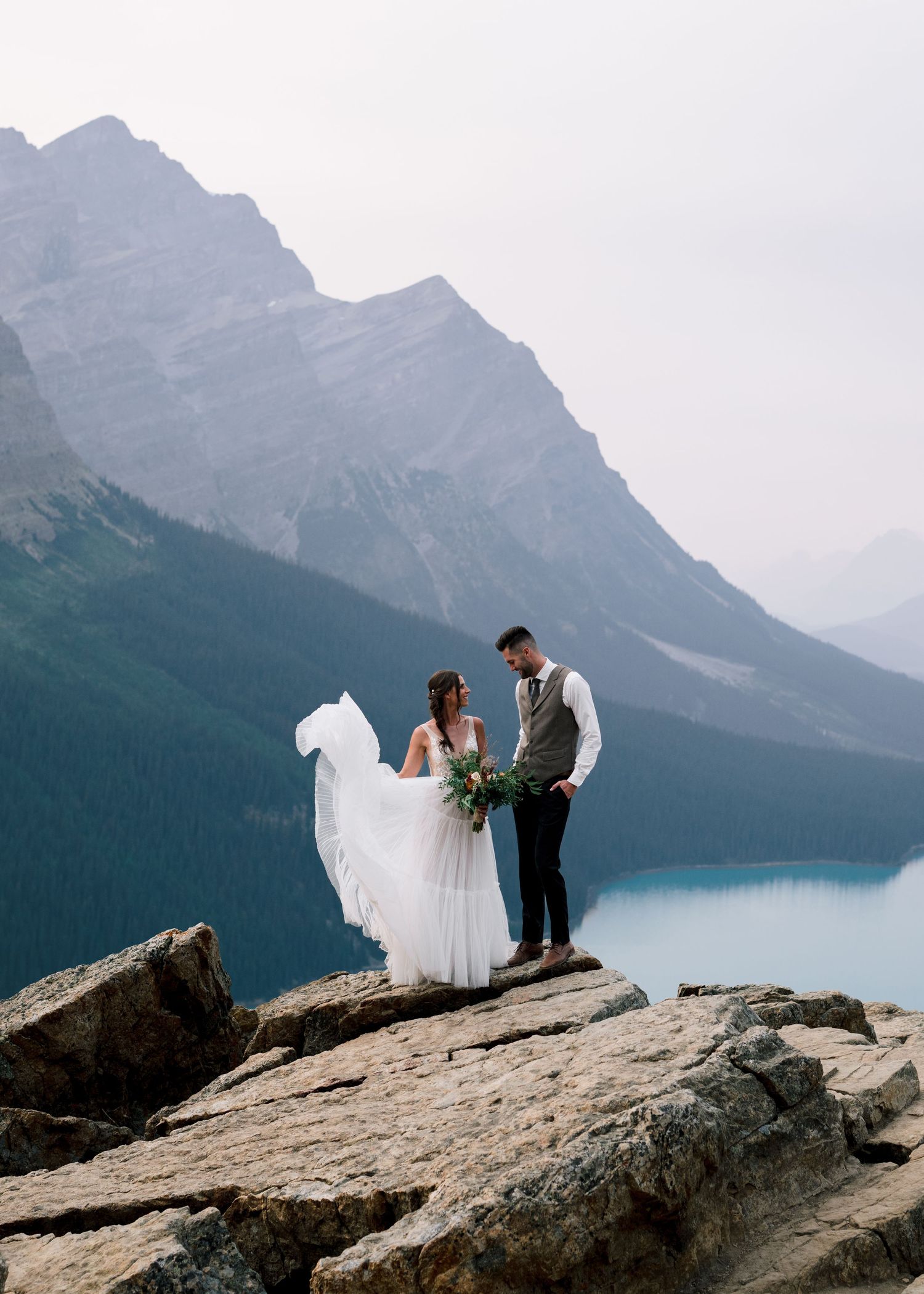 A couple sharing an intimate wedding moment on a rocky overlook above Lake Peyto in Banff National Park, Alberta.
