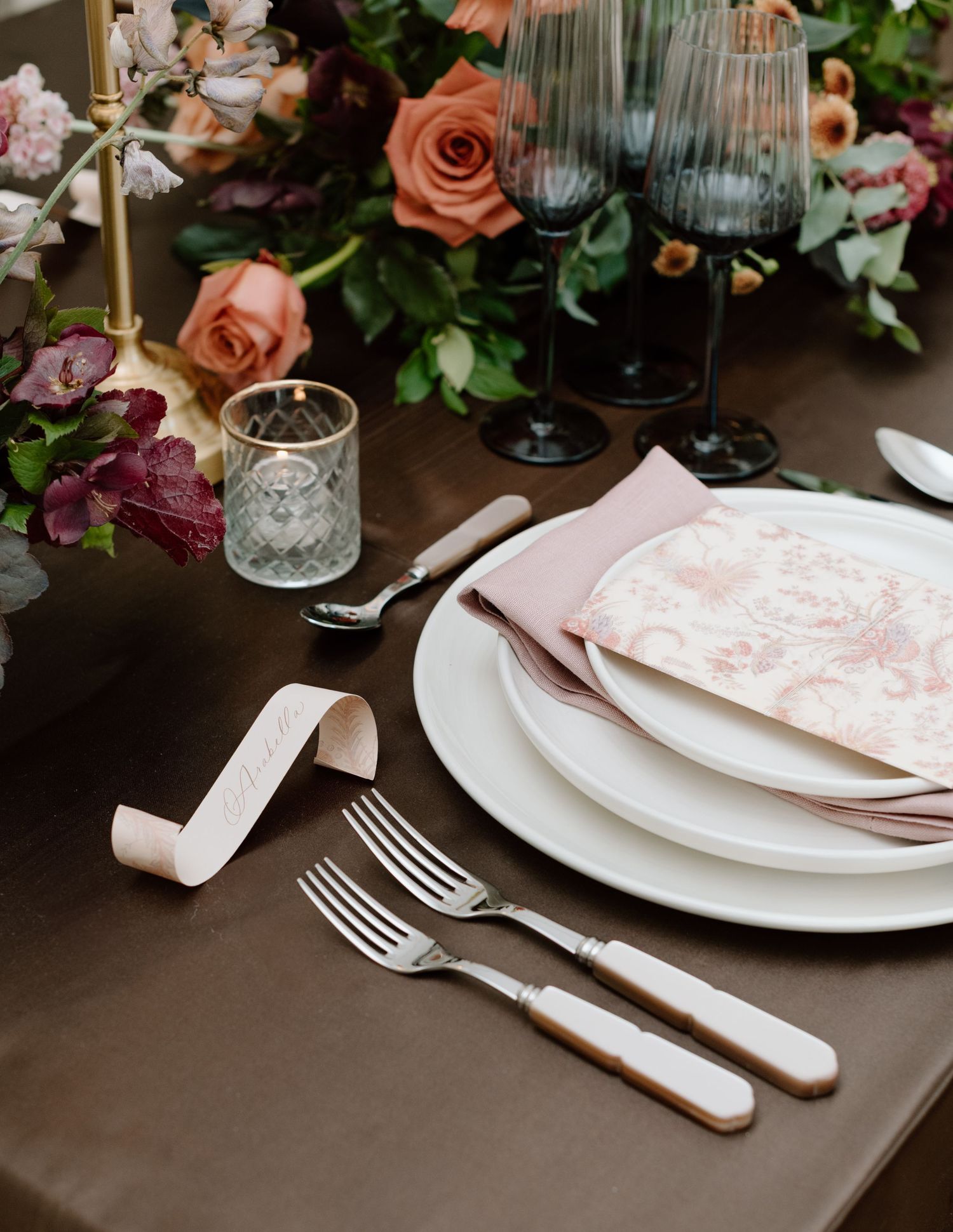 Elegant place setting with pink napkins, crystal glassware and coral roses on dark tablecloth at the Studio at Vic Park YYC Wedding Photo