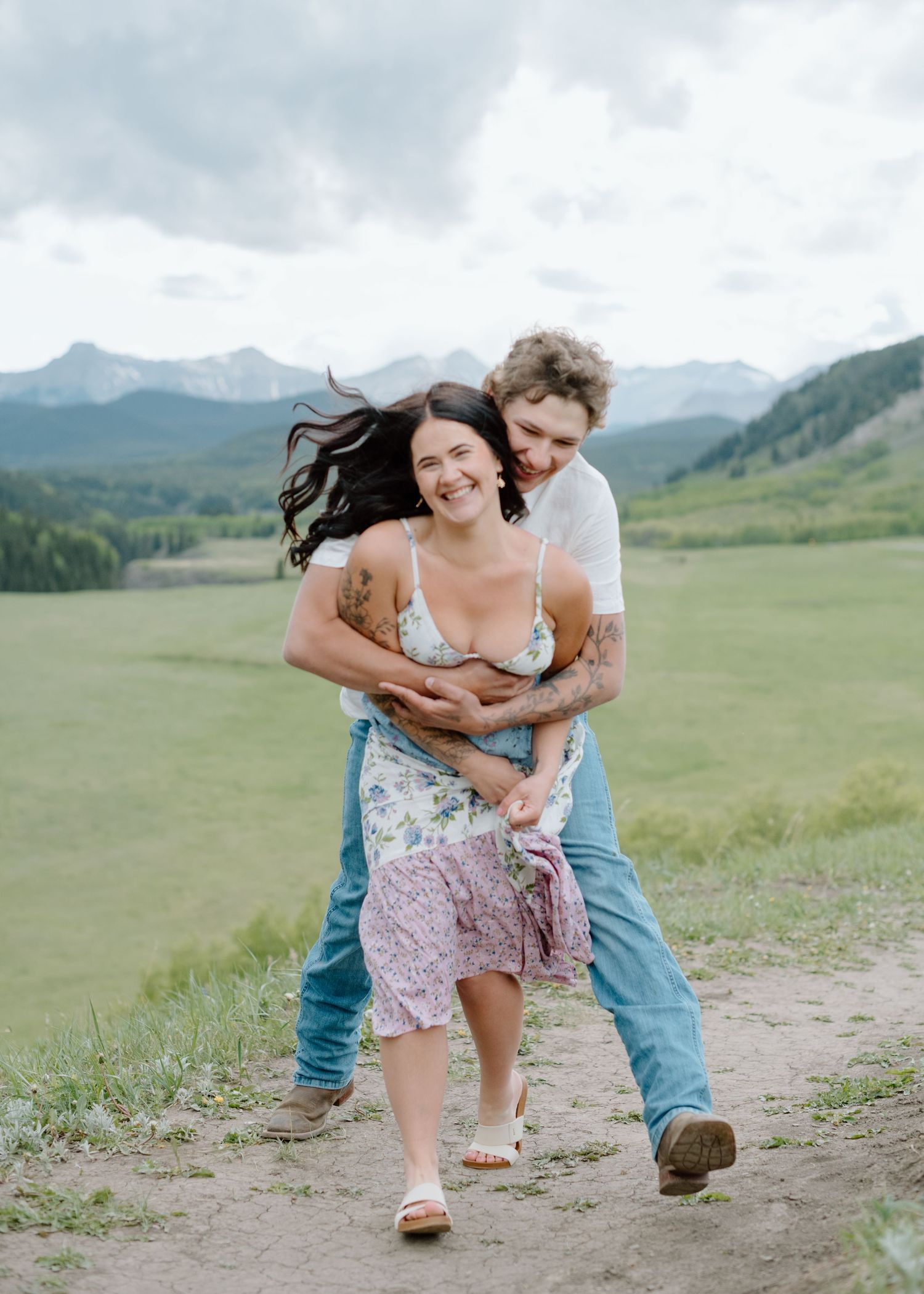 Couple running and playing together on a dirt path with scenic mountain views. Calgary Alberta Engagement Photographer.