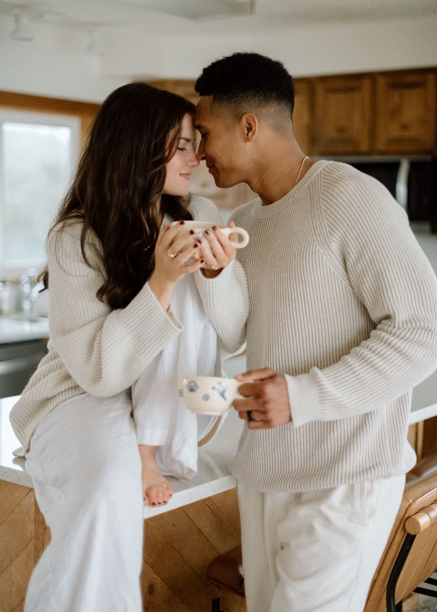 Couple in cozy white sweaters sharing intimate moments together in their kitchen.