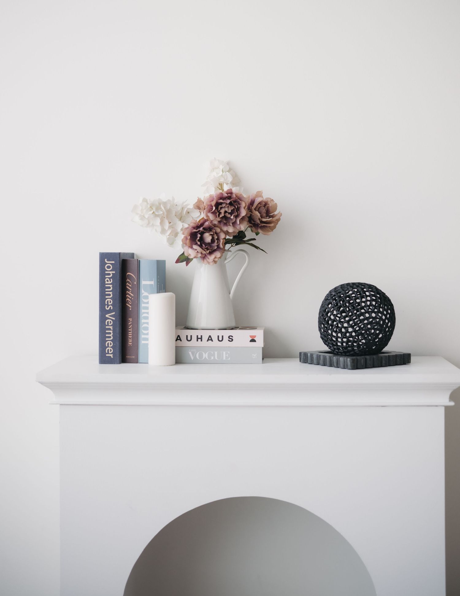 Minimalist white floating shelf styled with books, dried flowers, and decorative objects against a light gray wall.