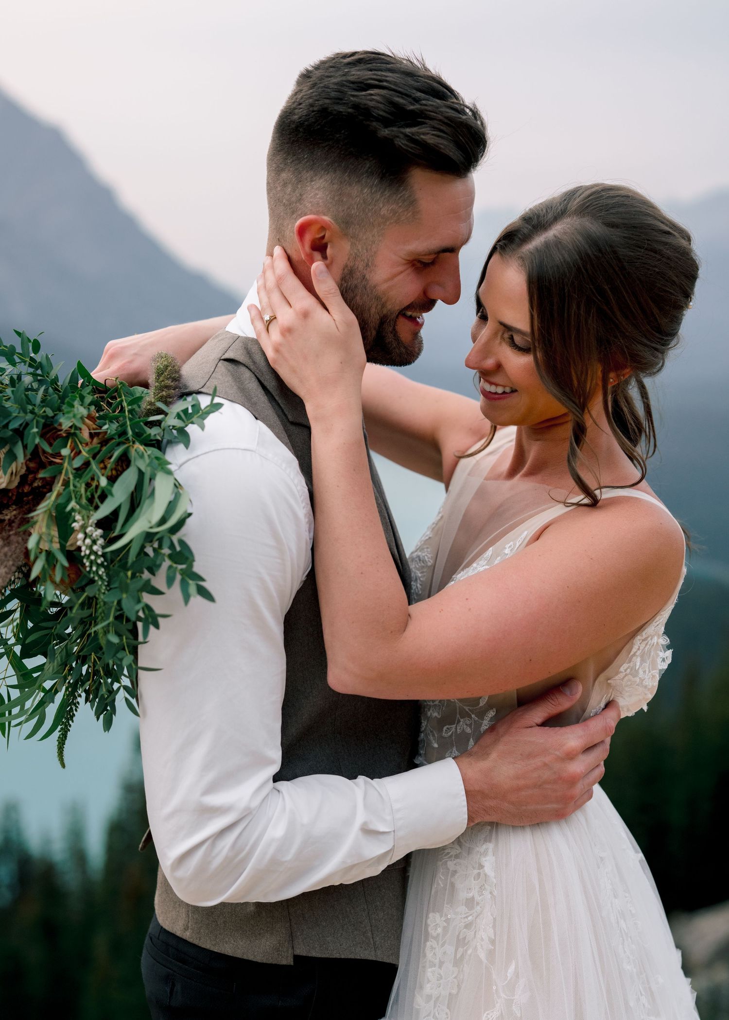 A couple shares intimate embrace during a wedding photoshoot with green foliage in the background.