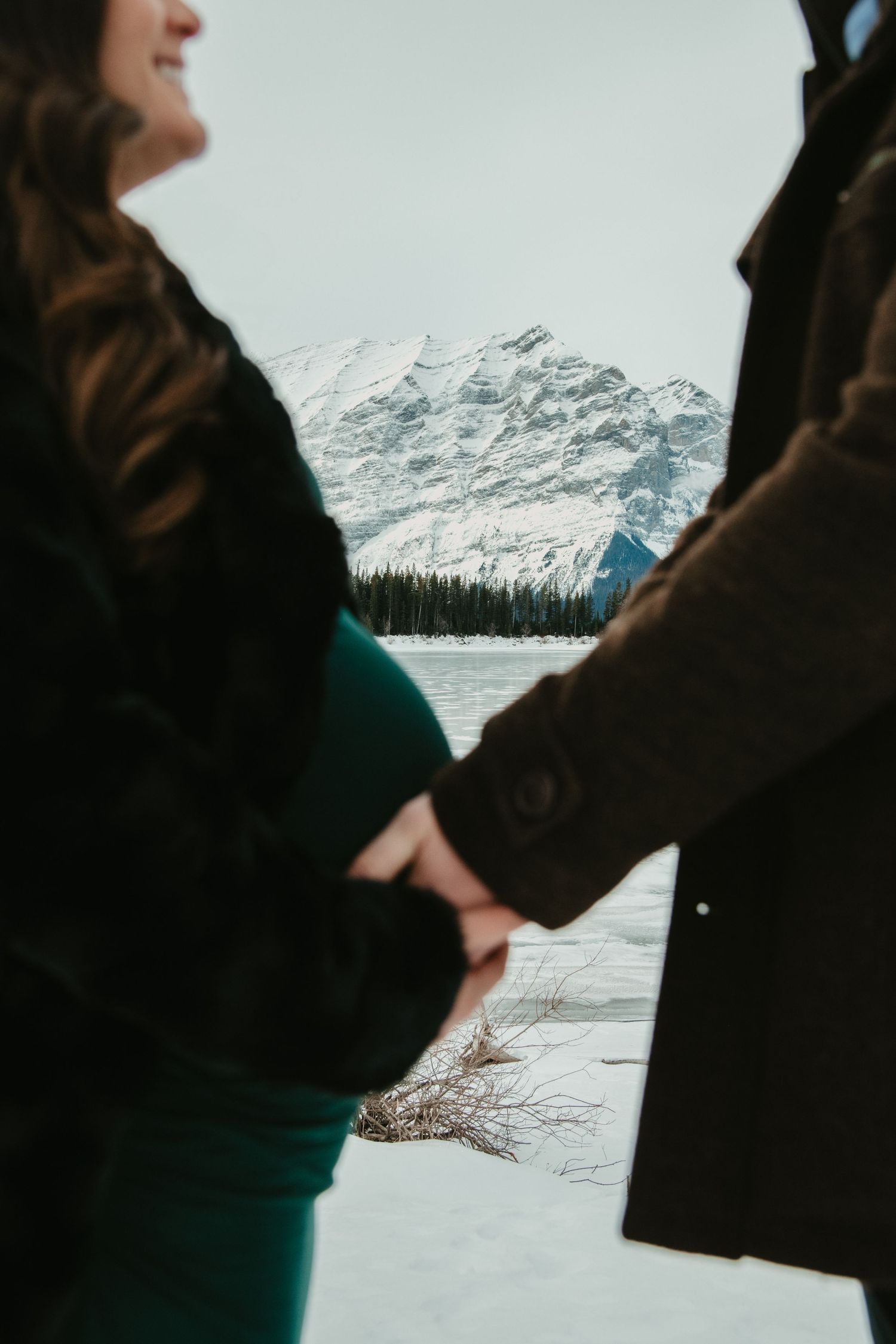 A silhouetted couple sharing an intimate moment against a backdrop of snow-covered mountains. Calgary Alberta Maternity Photographer.