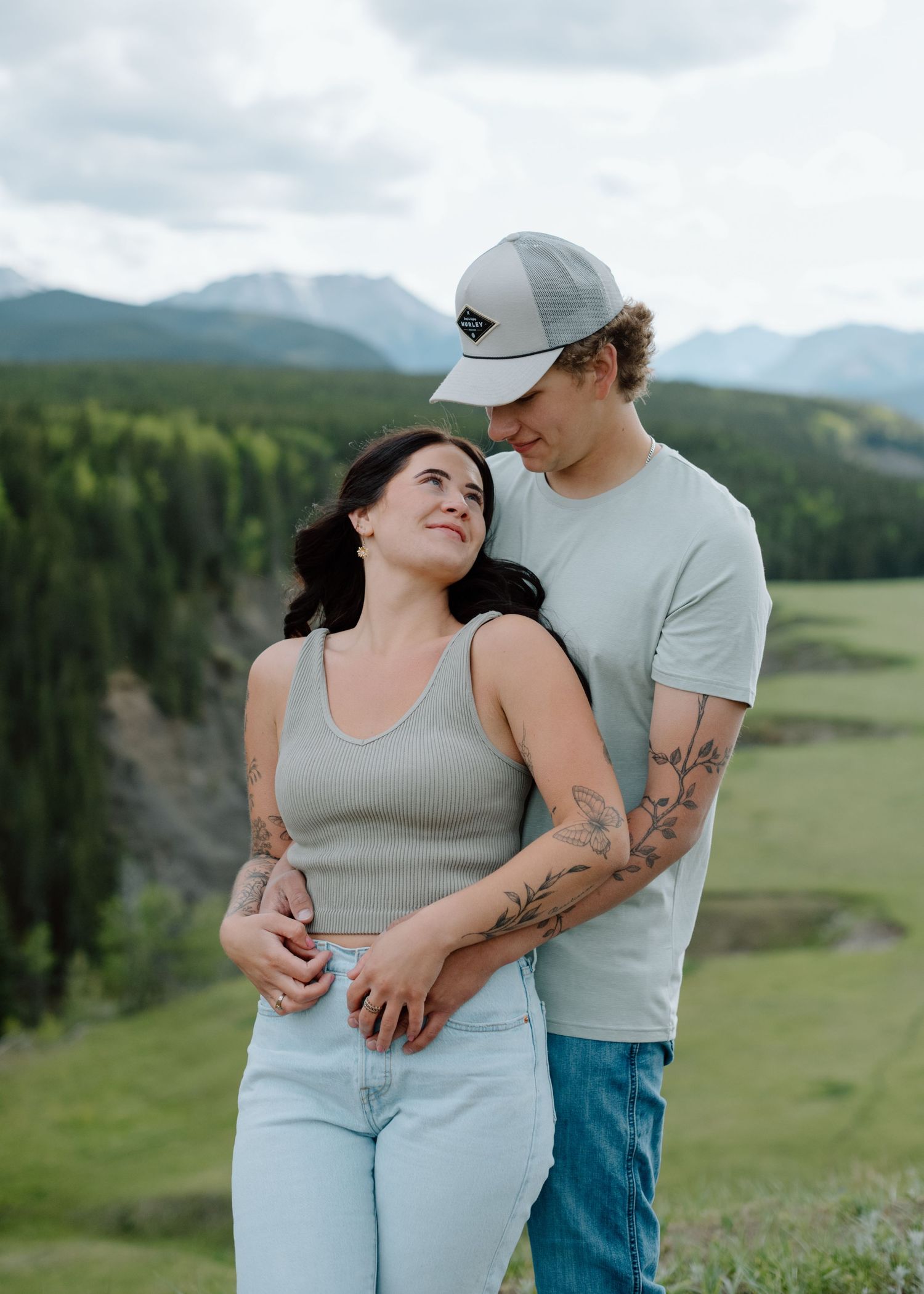 A couple in casual attire embracing on a scenic mountain overlook. Calgary Alberta Engagement Photographer.