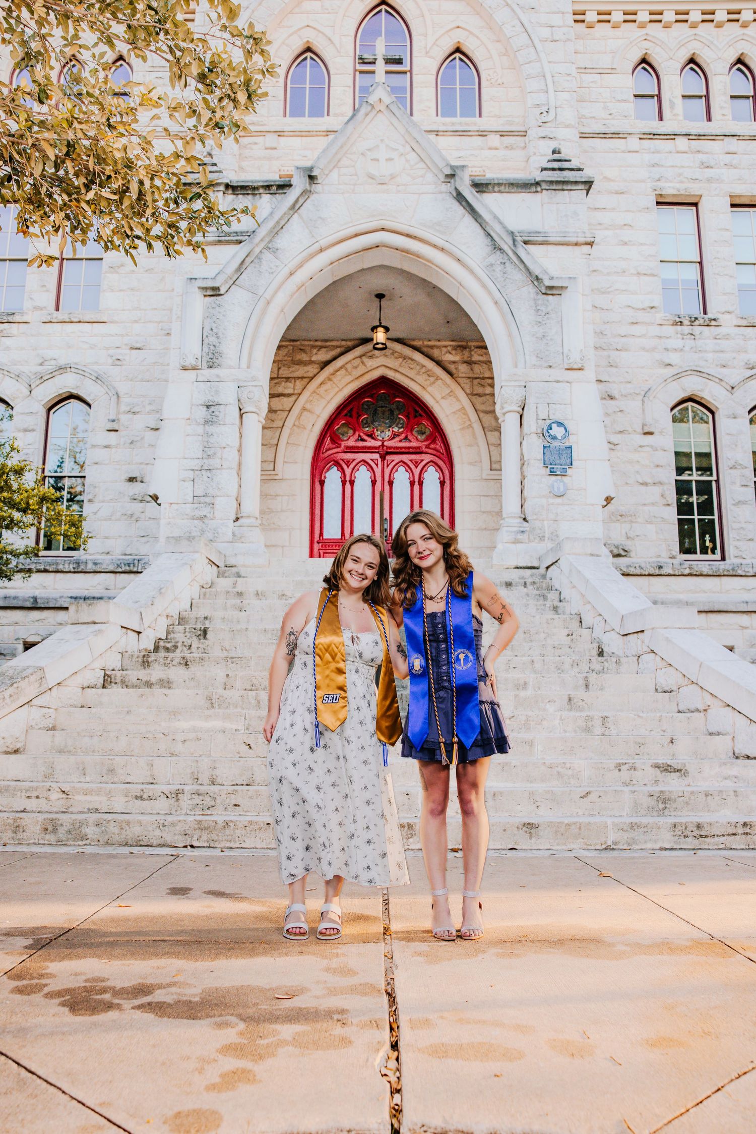 Two friends stand together in front of a historic stone church with a red door.