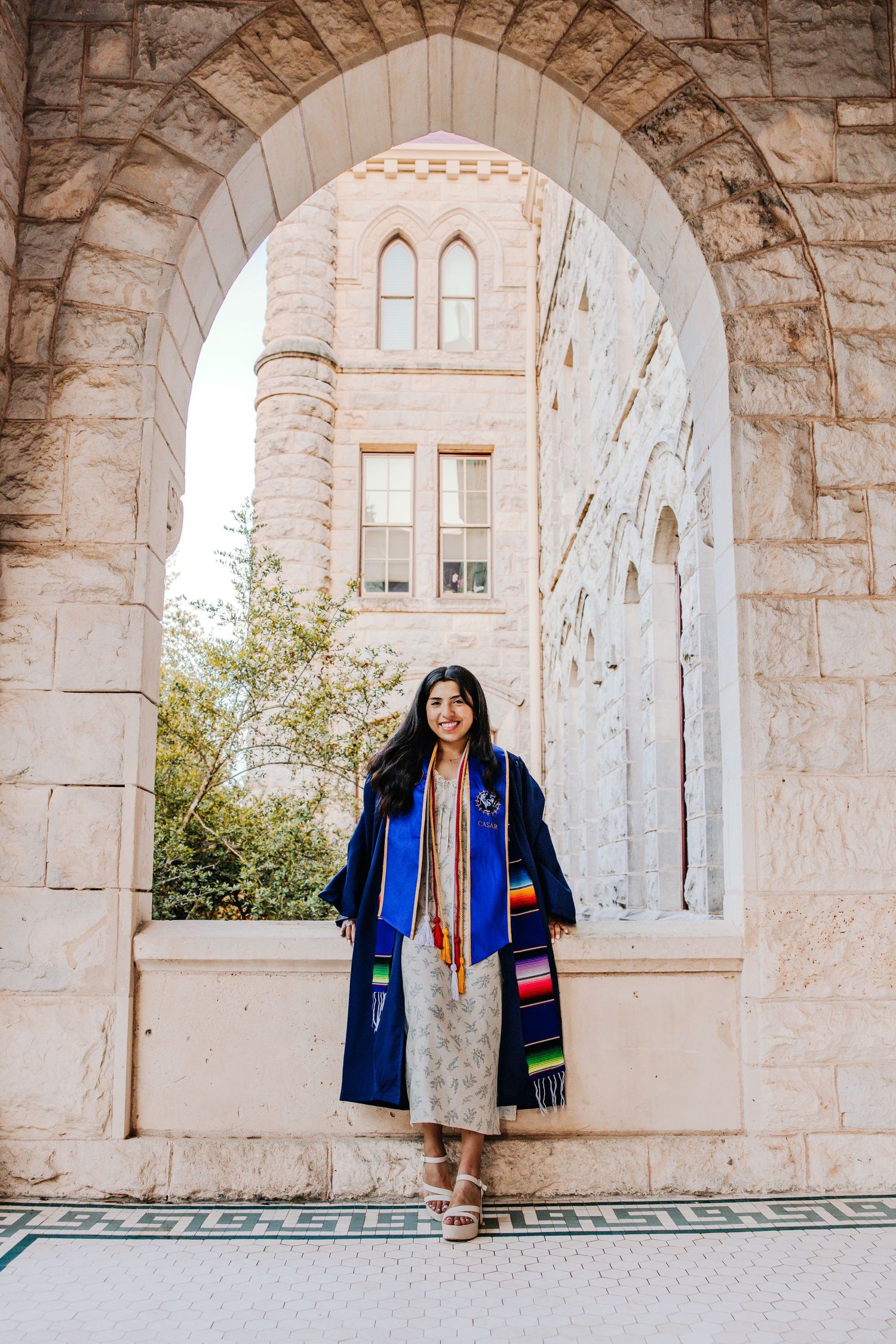 Graduate poses under stone archways of historic university architecture.