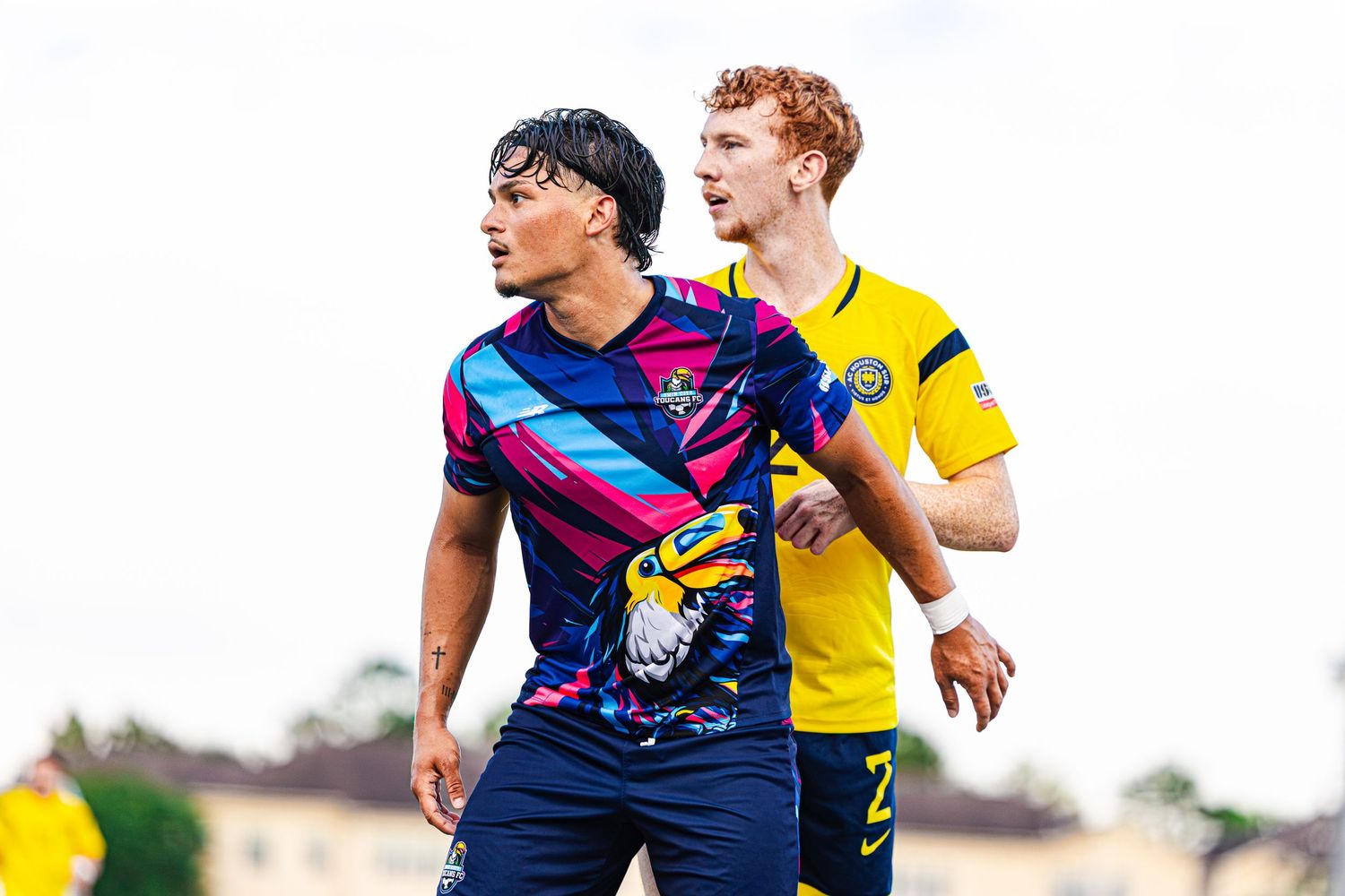 Two soccer players in colorful jerseys compete on a green field during a professional football match.