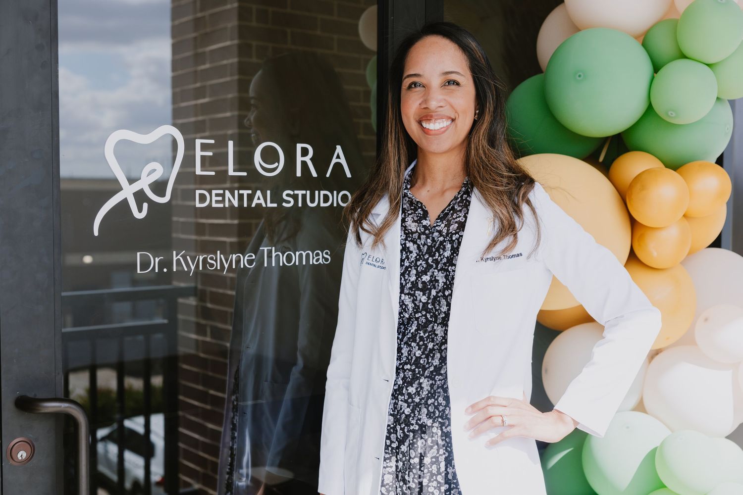Dental office exterior with white lab coat wearing professional standing by colorful balloon arch decoration.