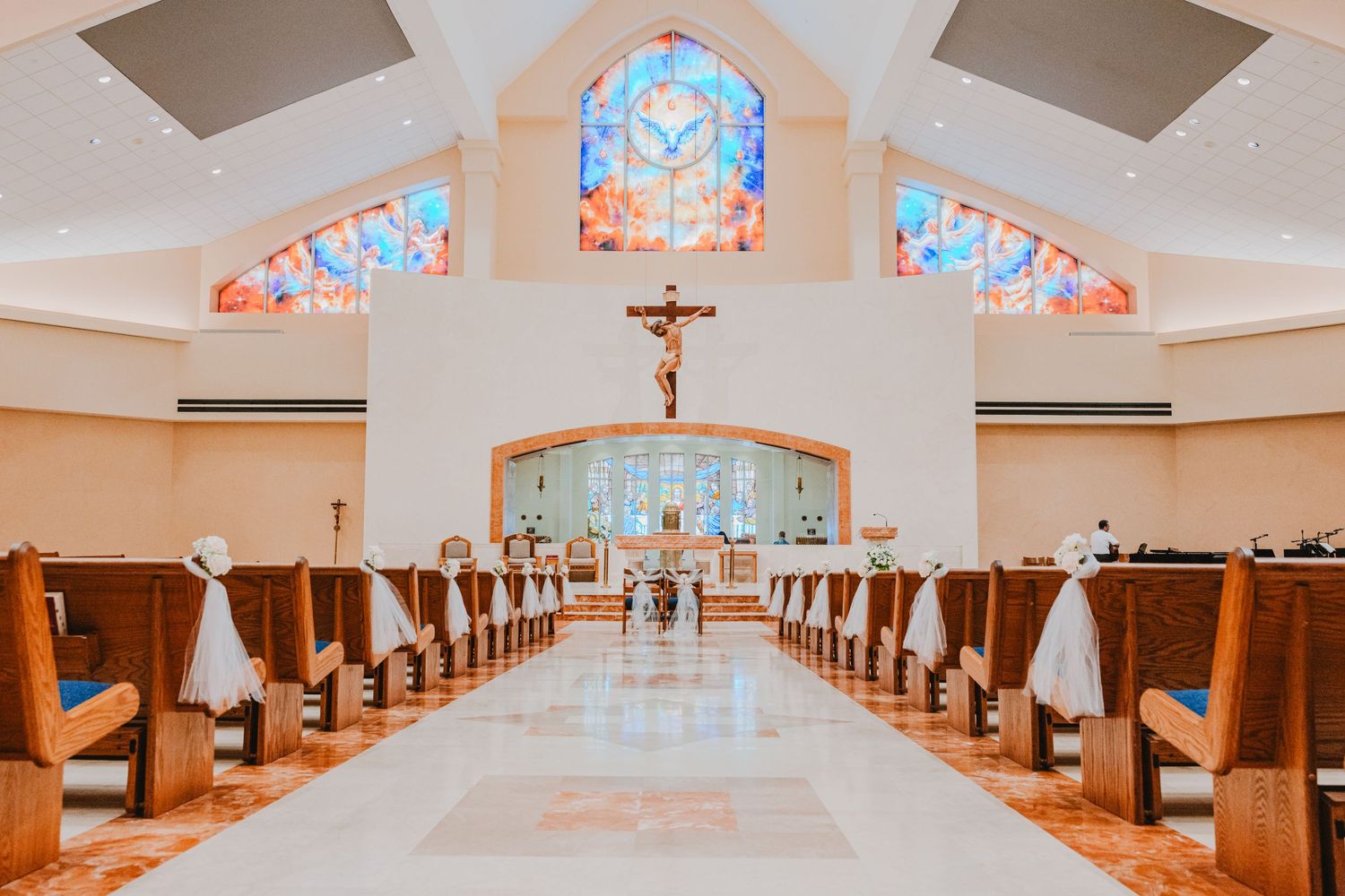 Elegant Catholic church interior with wooden pews, crucifix altar, and vibrant stained glass windows above.