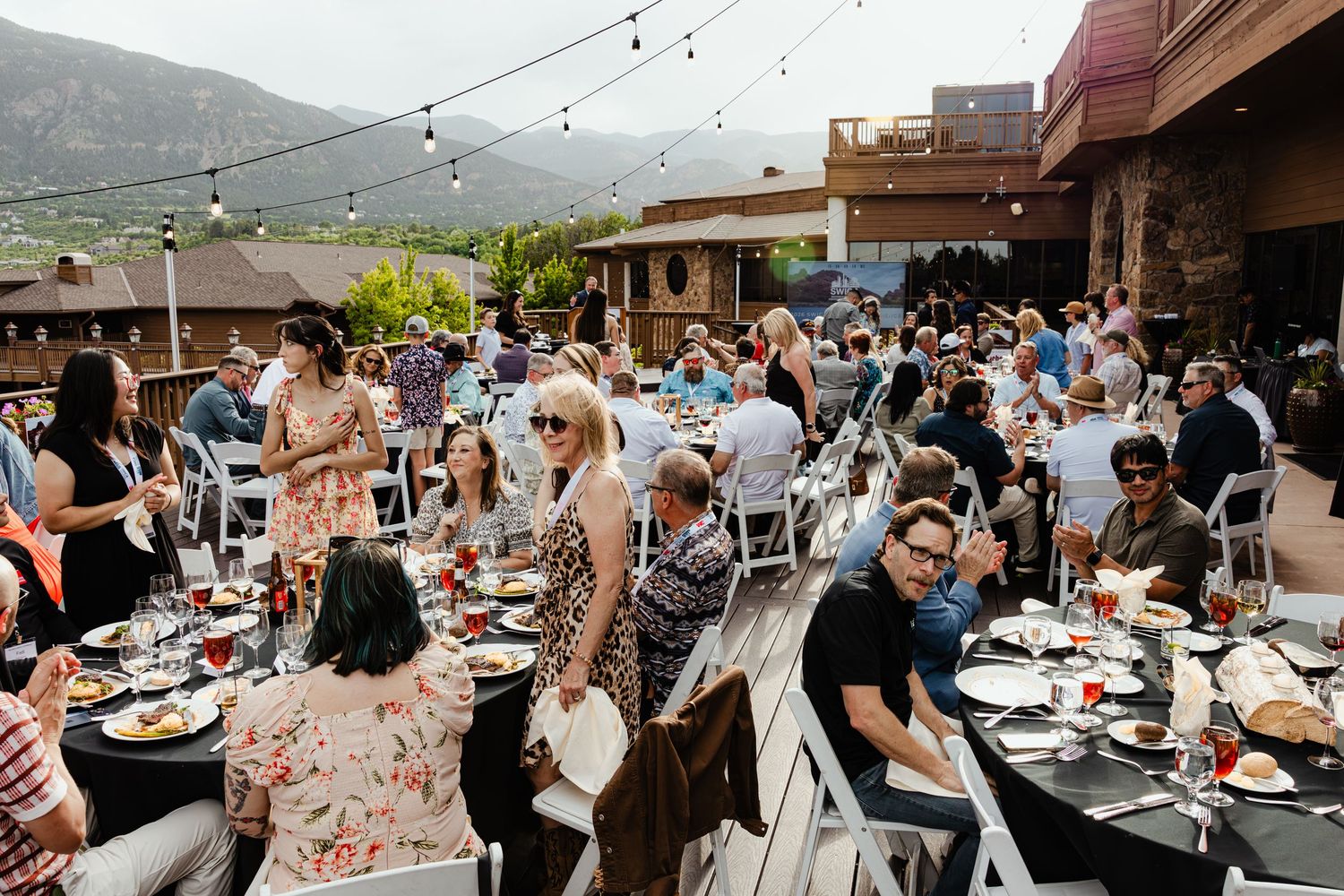 Guests dining outdoors at a mountain venue with string lights overhead during a festive group event.