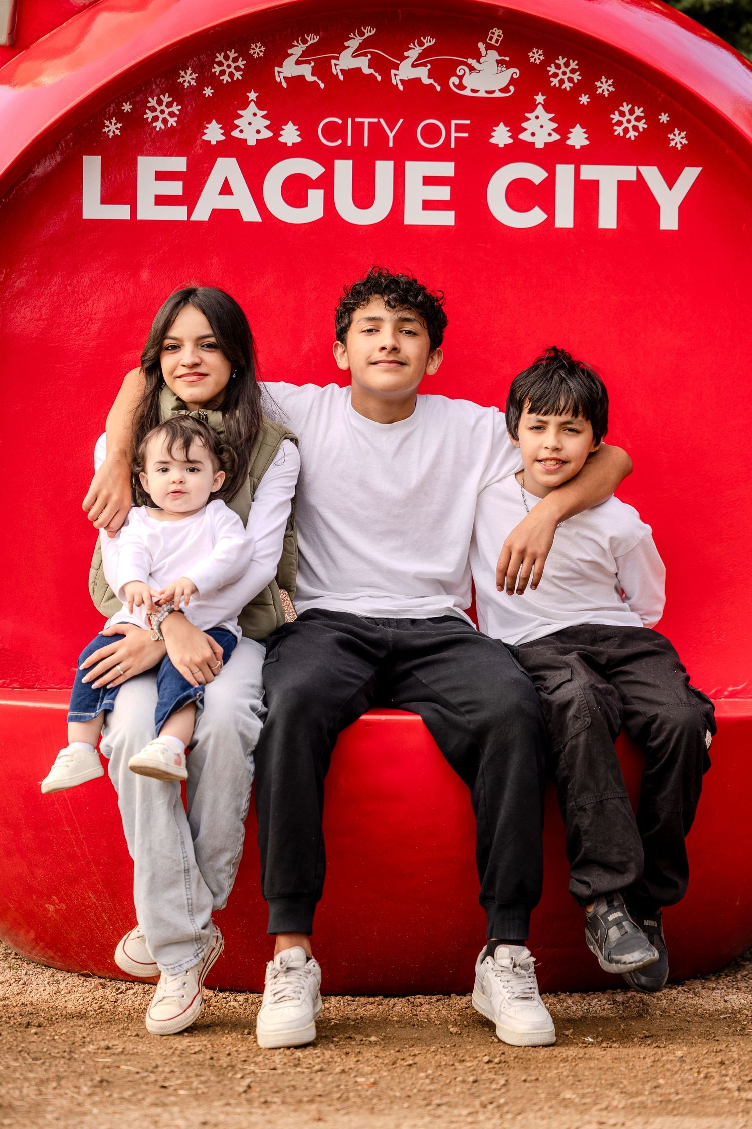 Three children sit together against a red curved wall with League City text visible in the background.