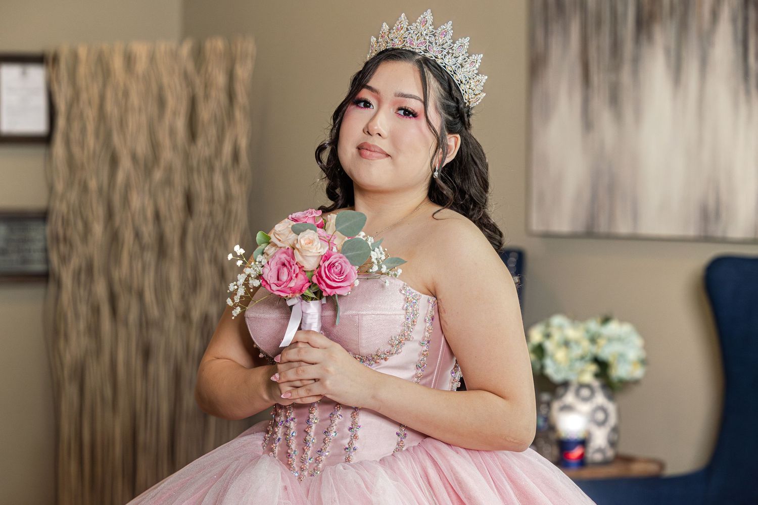 Young Latina girl in pink quinceañera ball gown with tiara holds bouquet of roses for her Sweet 15 celebration.