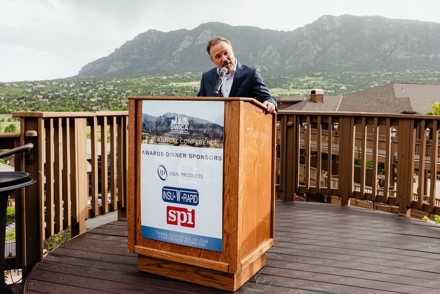Man speaking at outdoor podium with mountain backdrop at sponsored event near Boulder, Colorado.