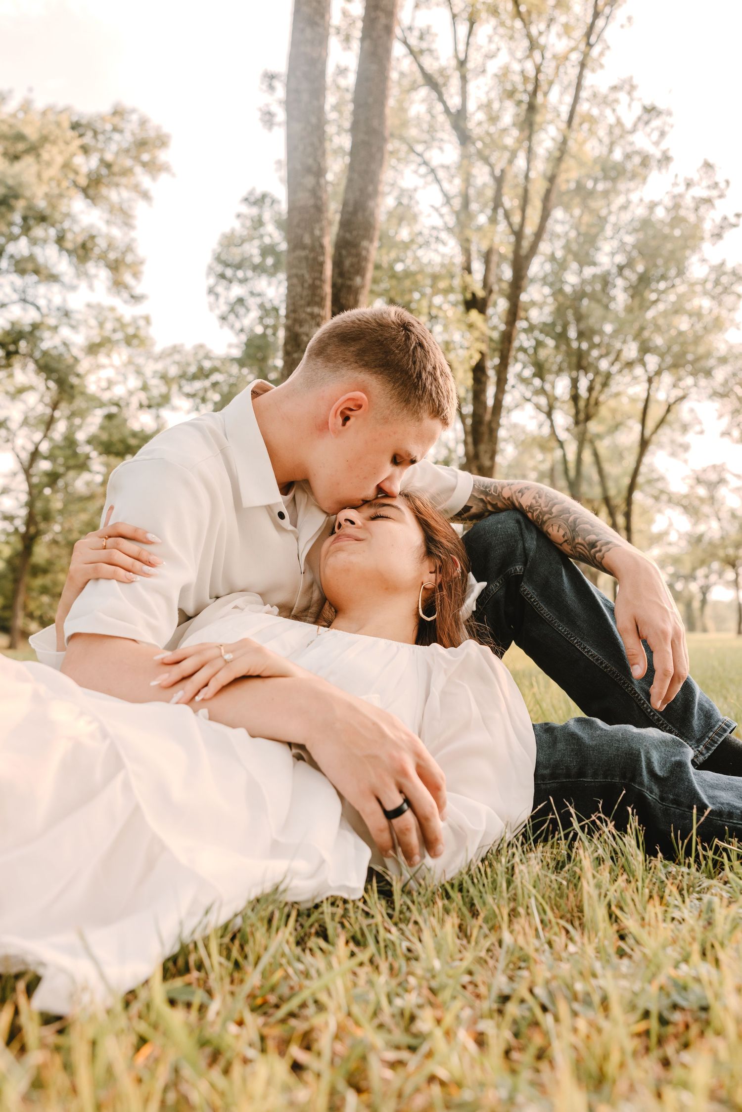 Romantic couple laying in tall grass at sunset sharing tender moments in a natural outdoor setting.
