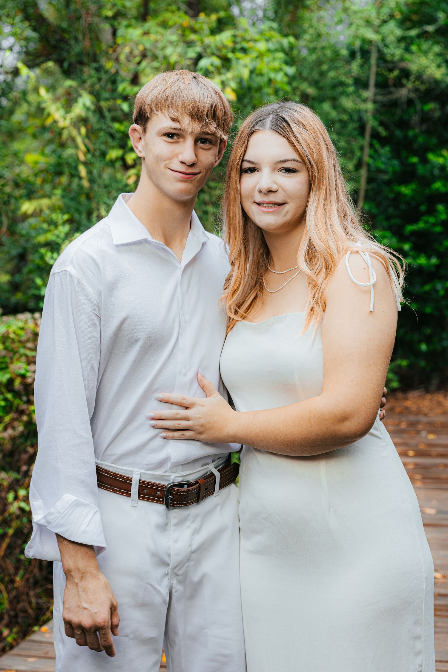 A couple in white attire poses together outdoors in a garden setting for romantic portraits.