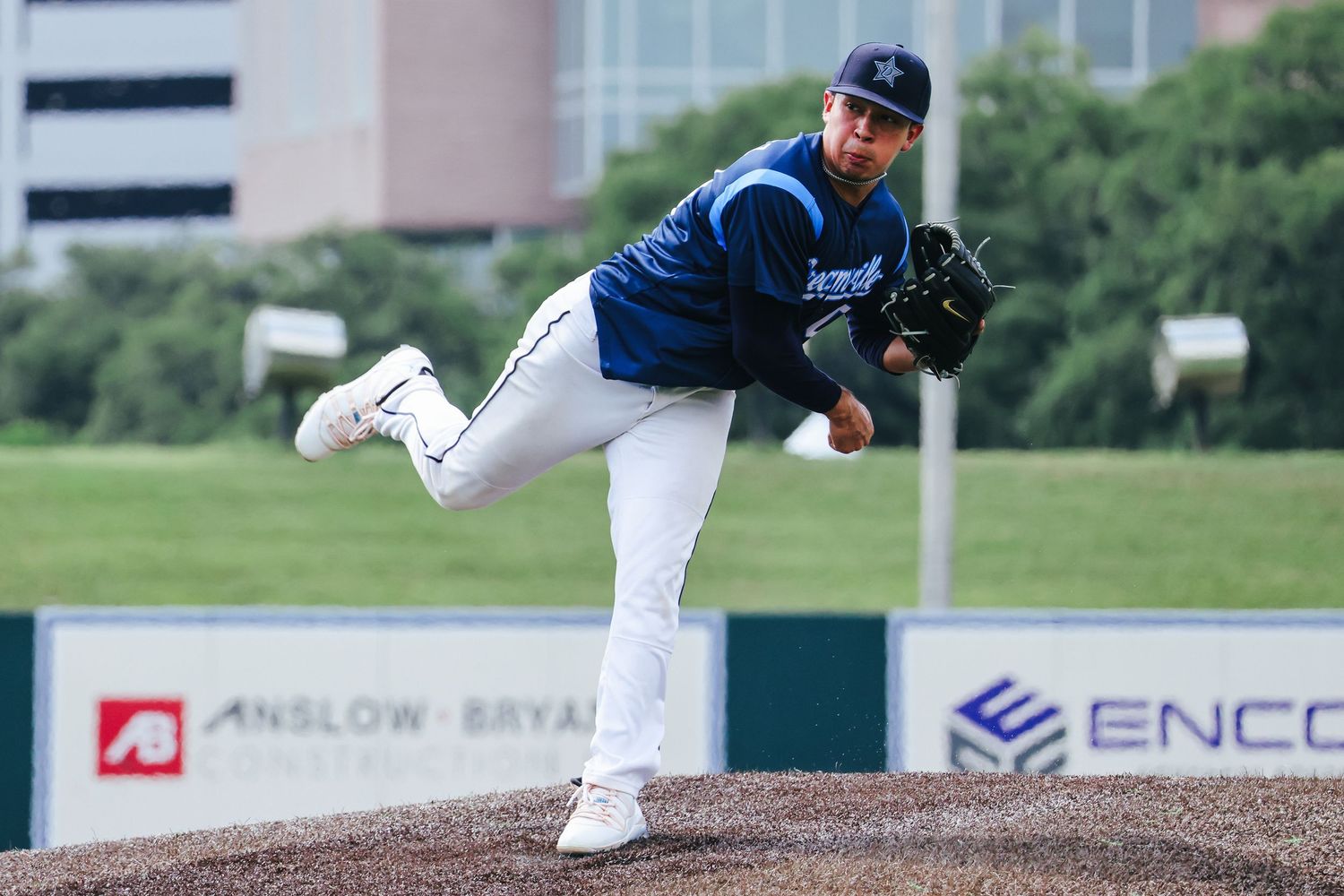 Baseball pitcher in blue uniform follows through on delivery from mound during game action.
