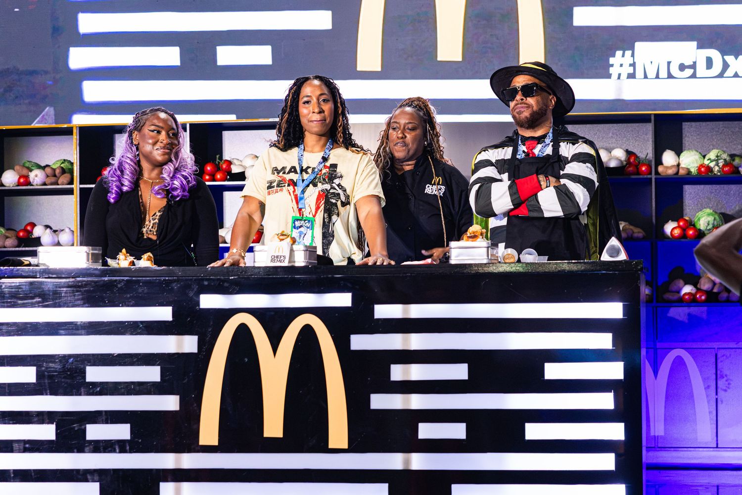 Four people stand behind a McDonald's branded DJ booth at a McDonalds promotional event.