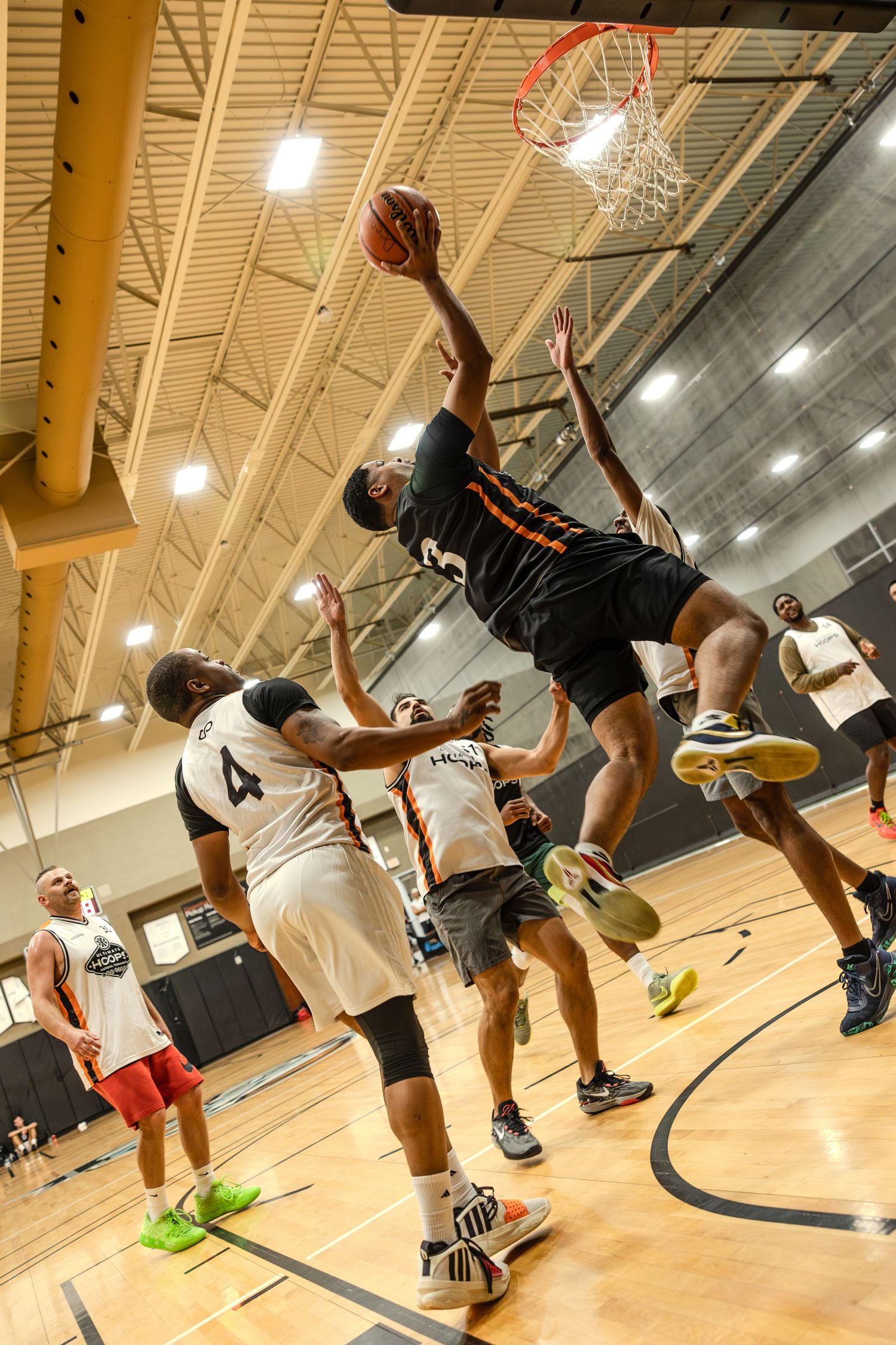 Basketball players leap high during an indoor practice session at a gymnasium with wooden floors and bright lighting.
