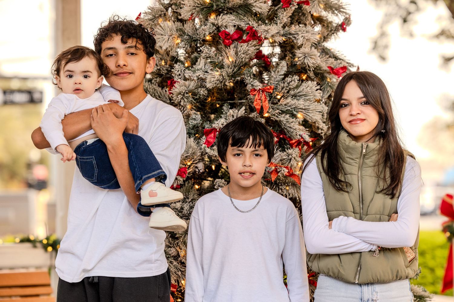 A group poses together in front of a decorated Christmas tree outdoors on a bright sunny day.