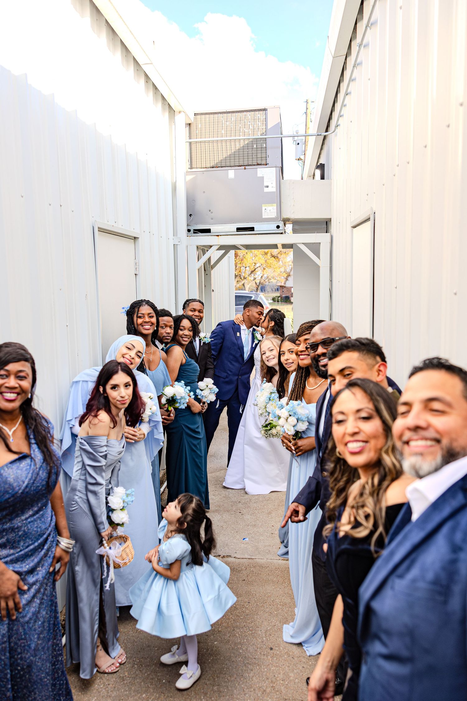 Wedding party celebrating in an outdoor corridor with joyful expressions and raised arms.