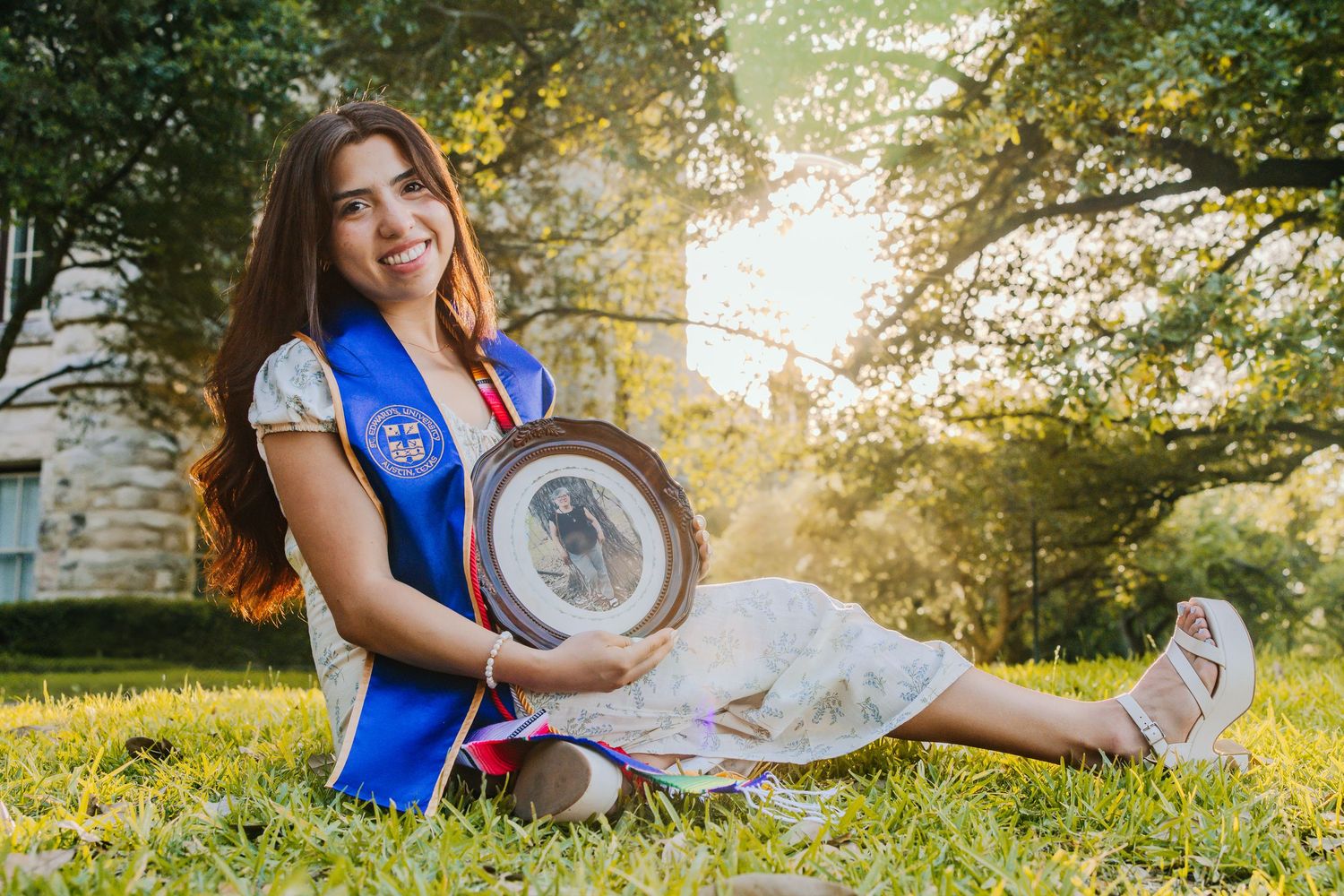 A person in a blue jersey sits on grass during golden hour sunset in a park setting.