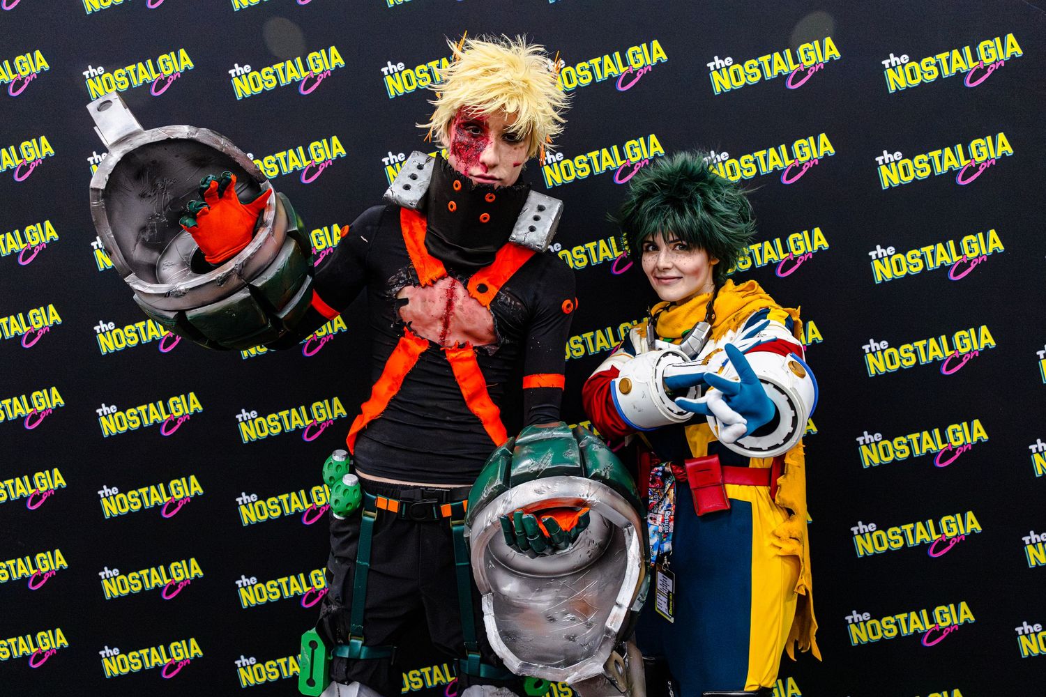 Two cosplayers dressed as My Hero Academia characters Bakugo and Deku pose at a Nostalgia convention.
