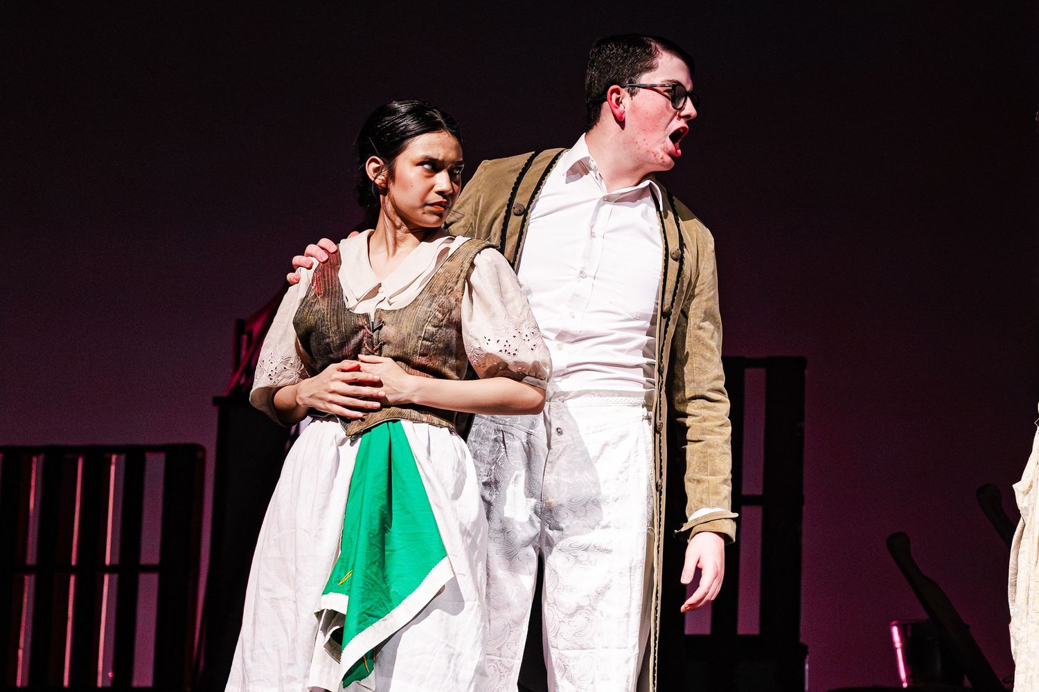 Two actors in period costumes perform an emotional scene on stage during a theater production.