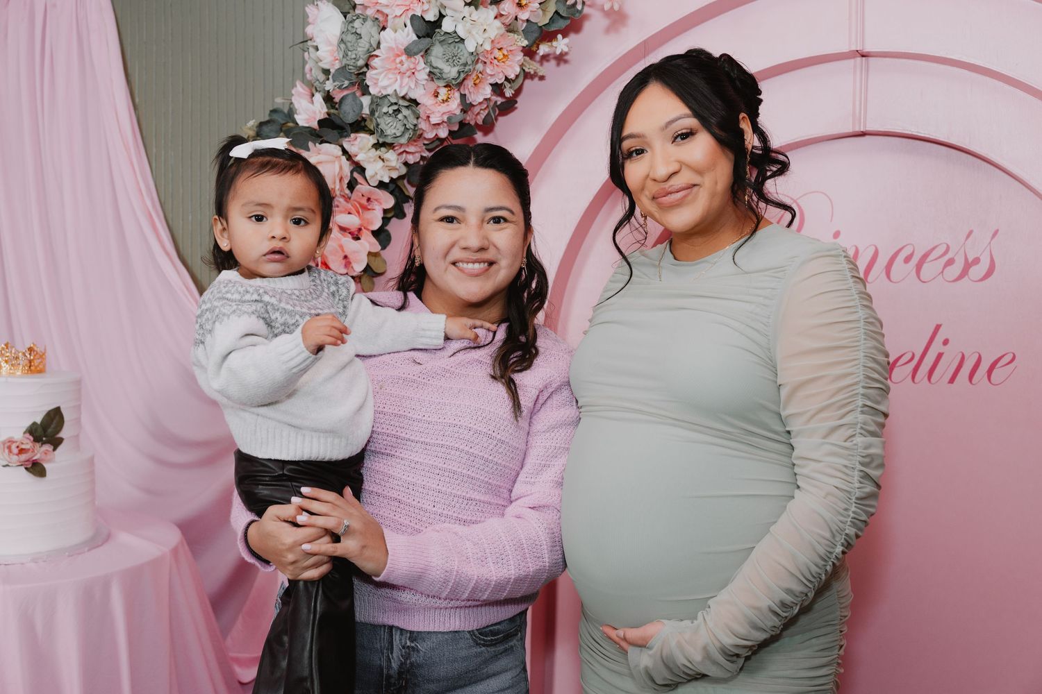 Pink floral backdrop with people posing in coordinated pink and white outfits for a celebration or photoshoot.
