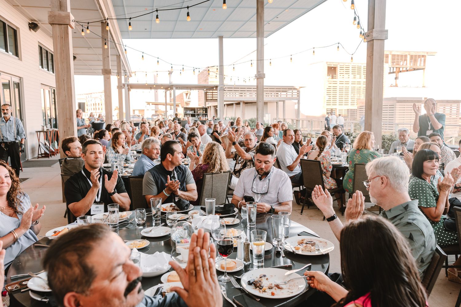 Large crowd gathered at an indoor event venue with string lights and tables.