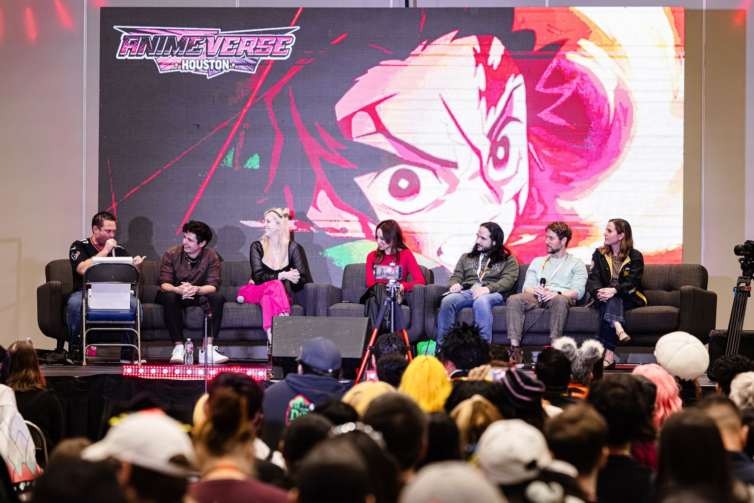 A panel of speakers discuss anime on stage at an Animeverse convention event.