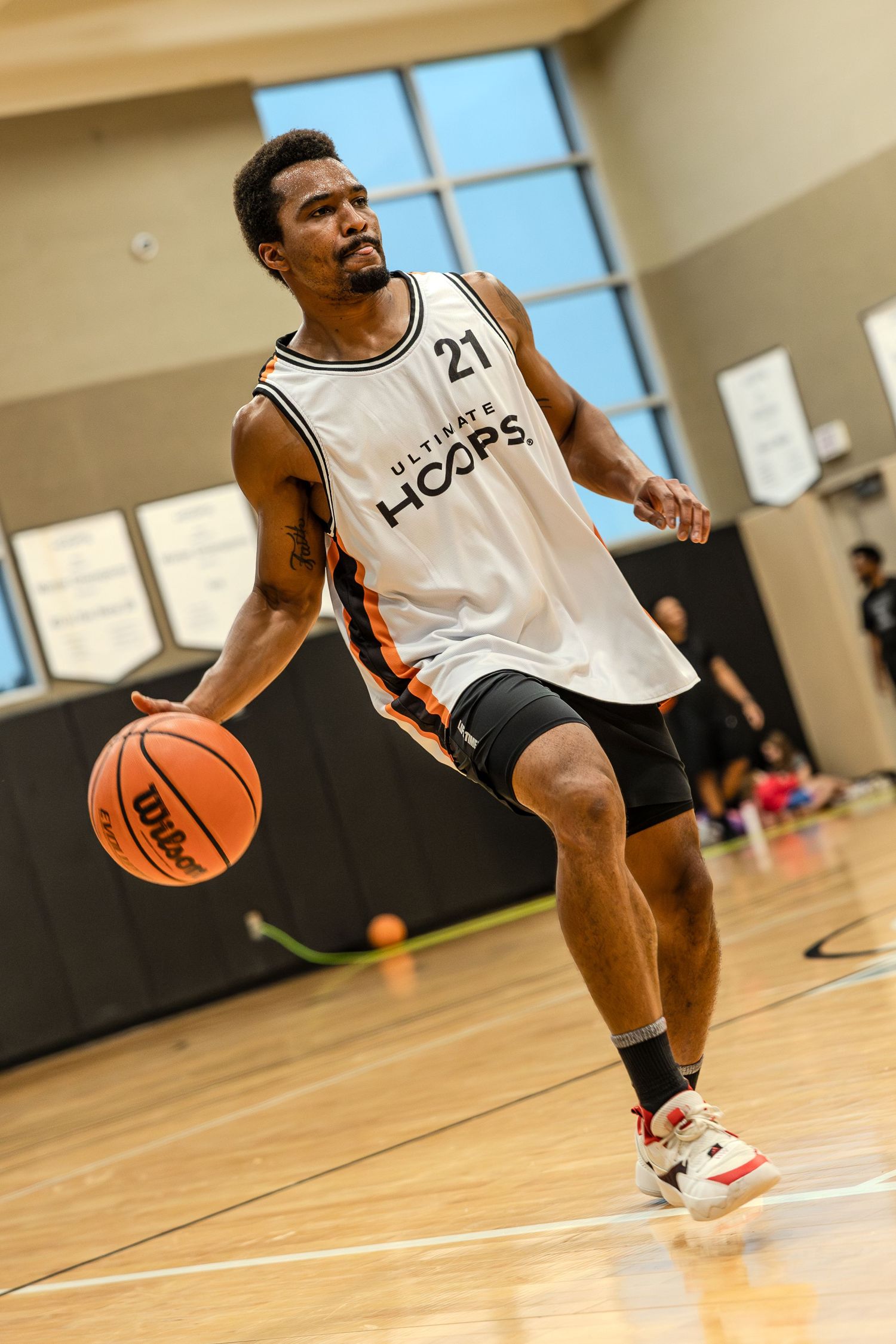 Basketball player dribbles low on wooden court during indoor game wearing white jersey with number 21.