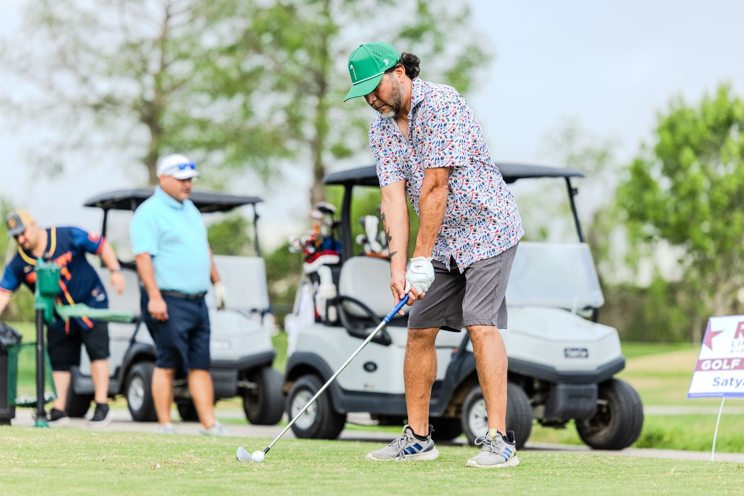 Golfers and golf carts spread across a lush green golf course during a sunny day.