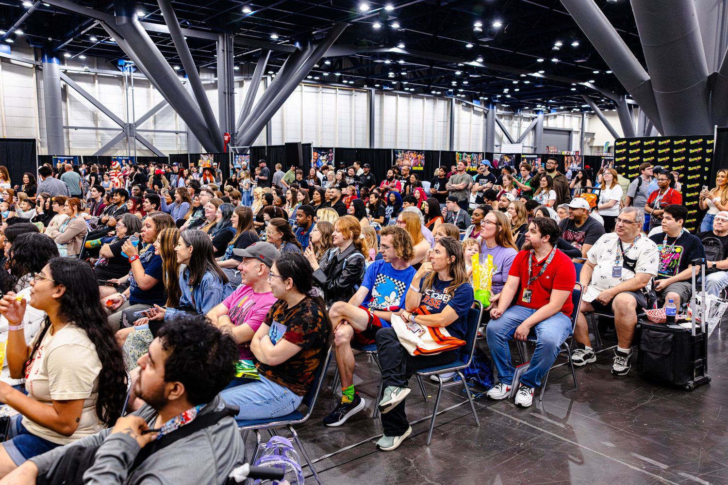 Large crowd of attendees sitting in chairs at an indoor convention hall during a panel event.