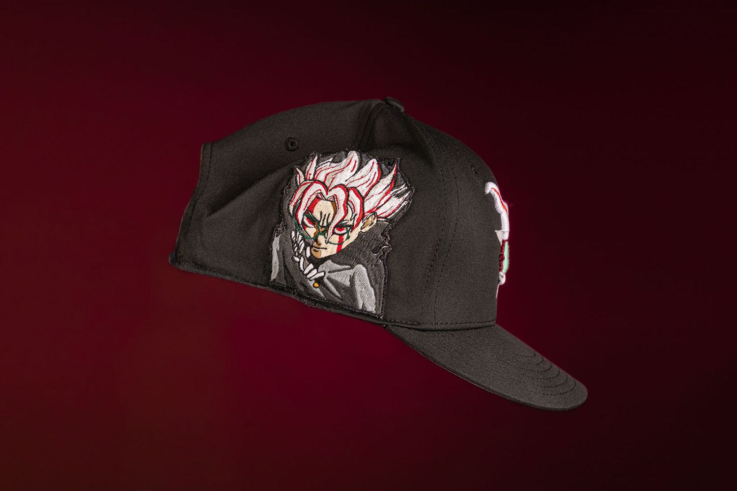 Black snapback cap featuring anime character artwork with red and white details on dark background.