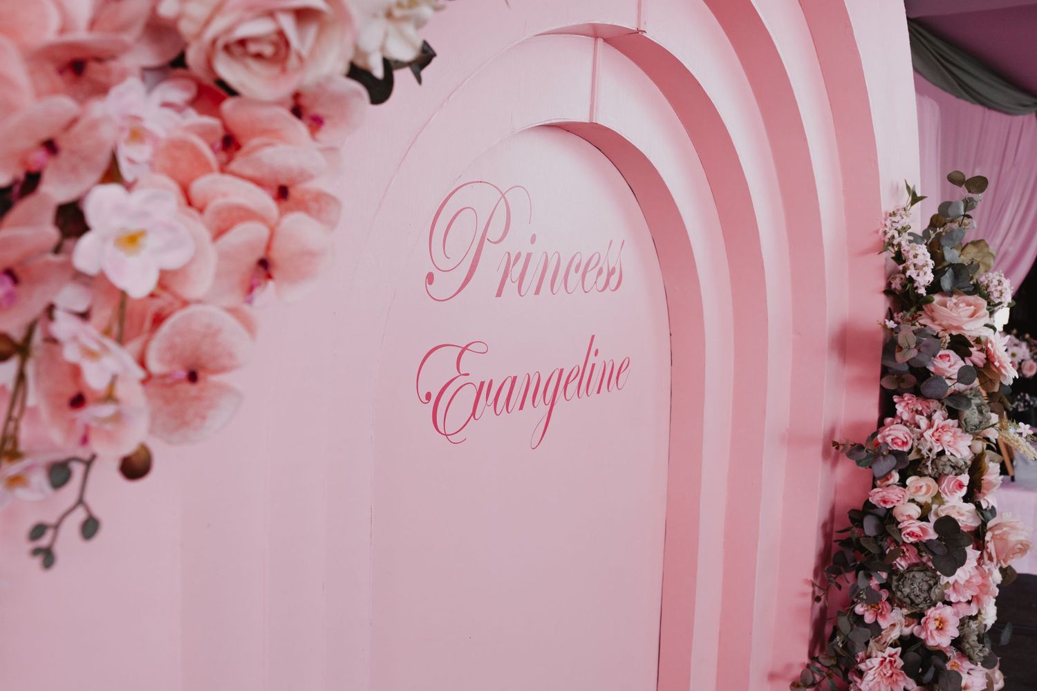 Pink and white floral decorations against a striped pink and white backdrop create an elegant party setting.