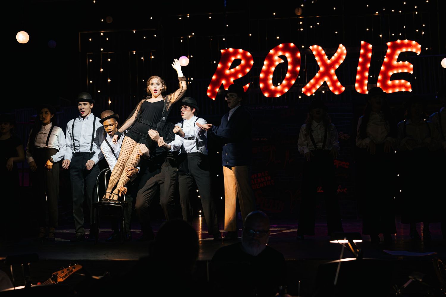Performers on stage with illuminated red 'POXIE' sign glowing in the background during nighttime show.