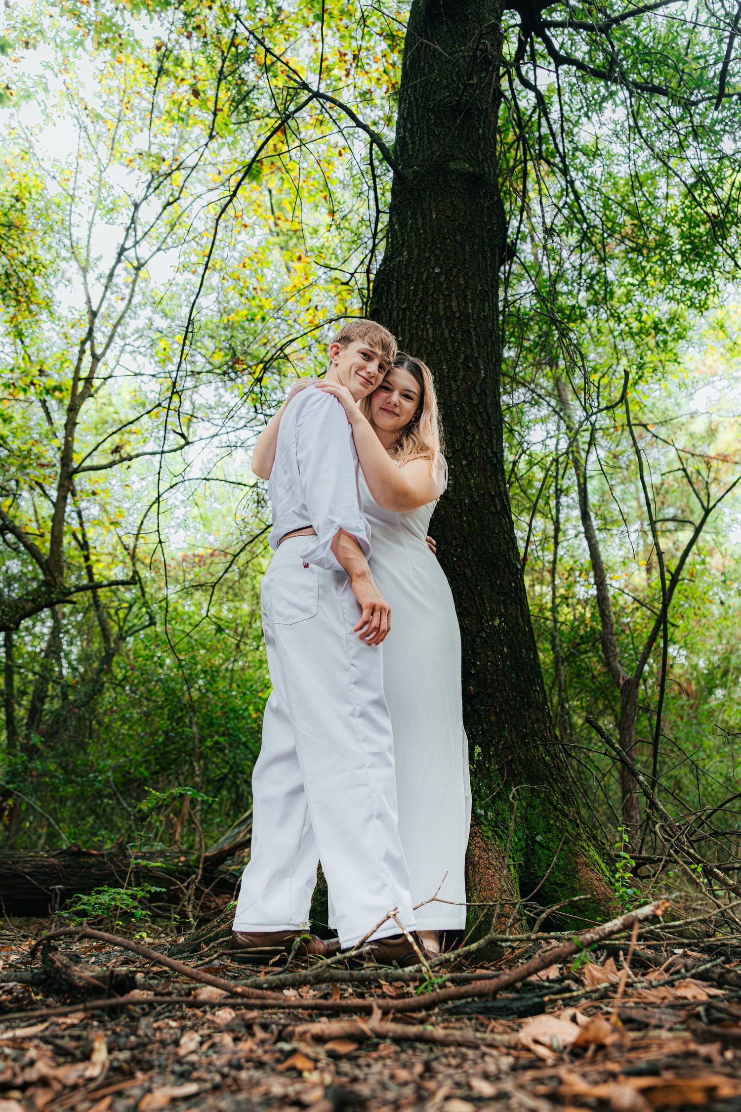 White clothing and shoes visible against natural forest floor background with trees and green foliage in sunlight.