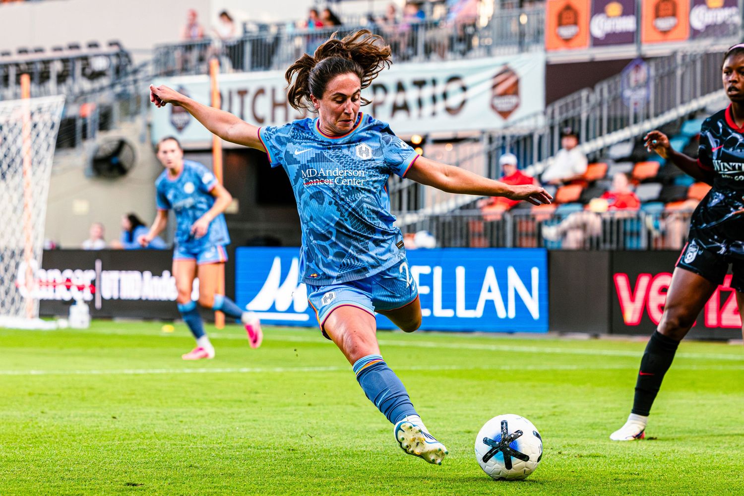 Female soccer player in blue uniform executing a powerful kick during a professional women's soccer match.