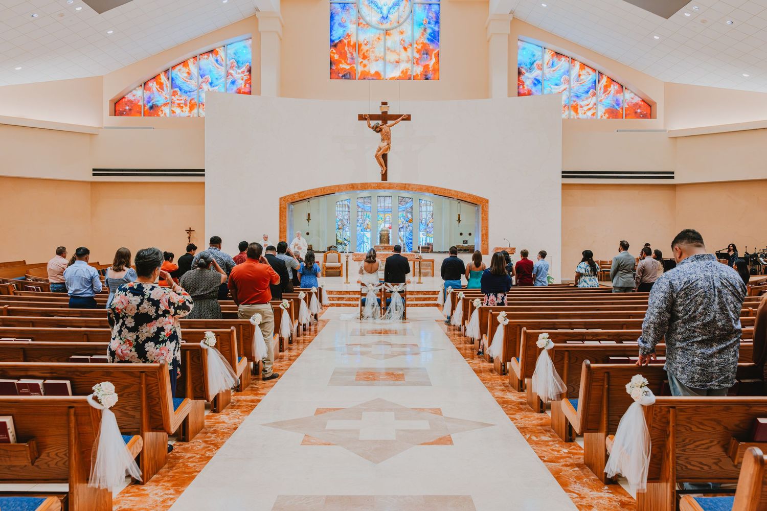 A church sanctuary interior with wooden pews and stained glass windows illuminated in warm lighting.