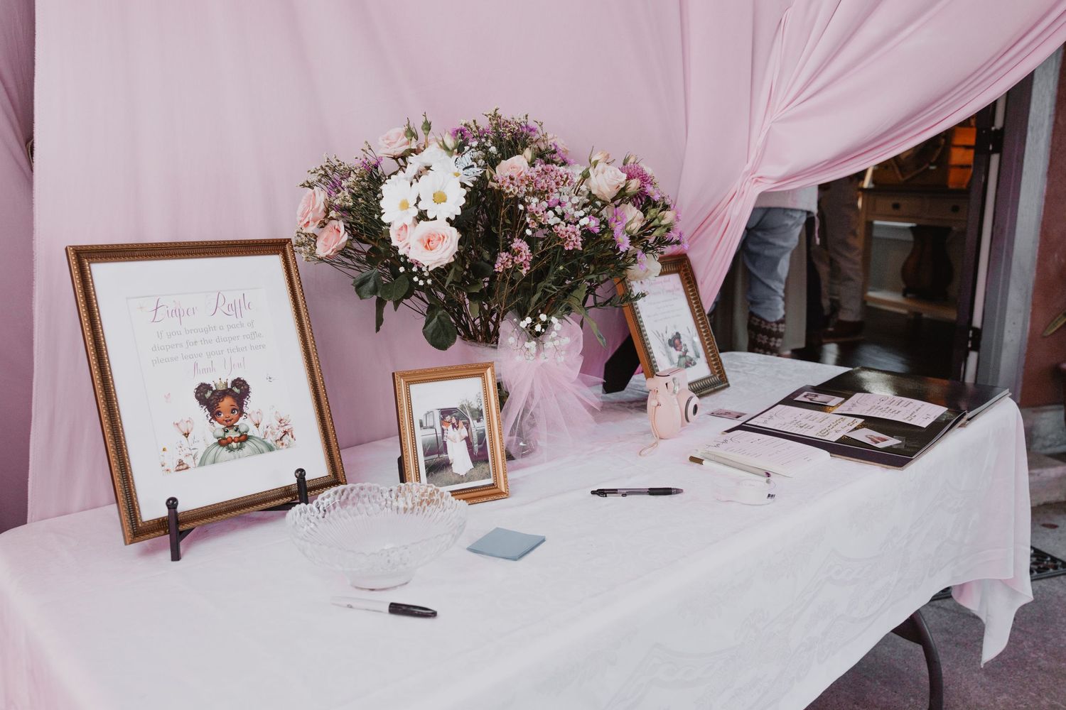 A romantic pink and white wedding reception setup with draped fabric, floral arrangements, and framed photos on display.