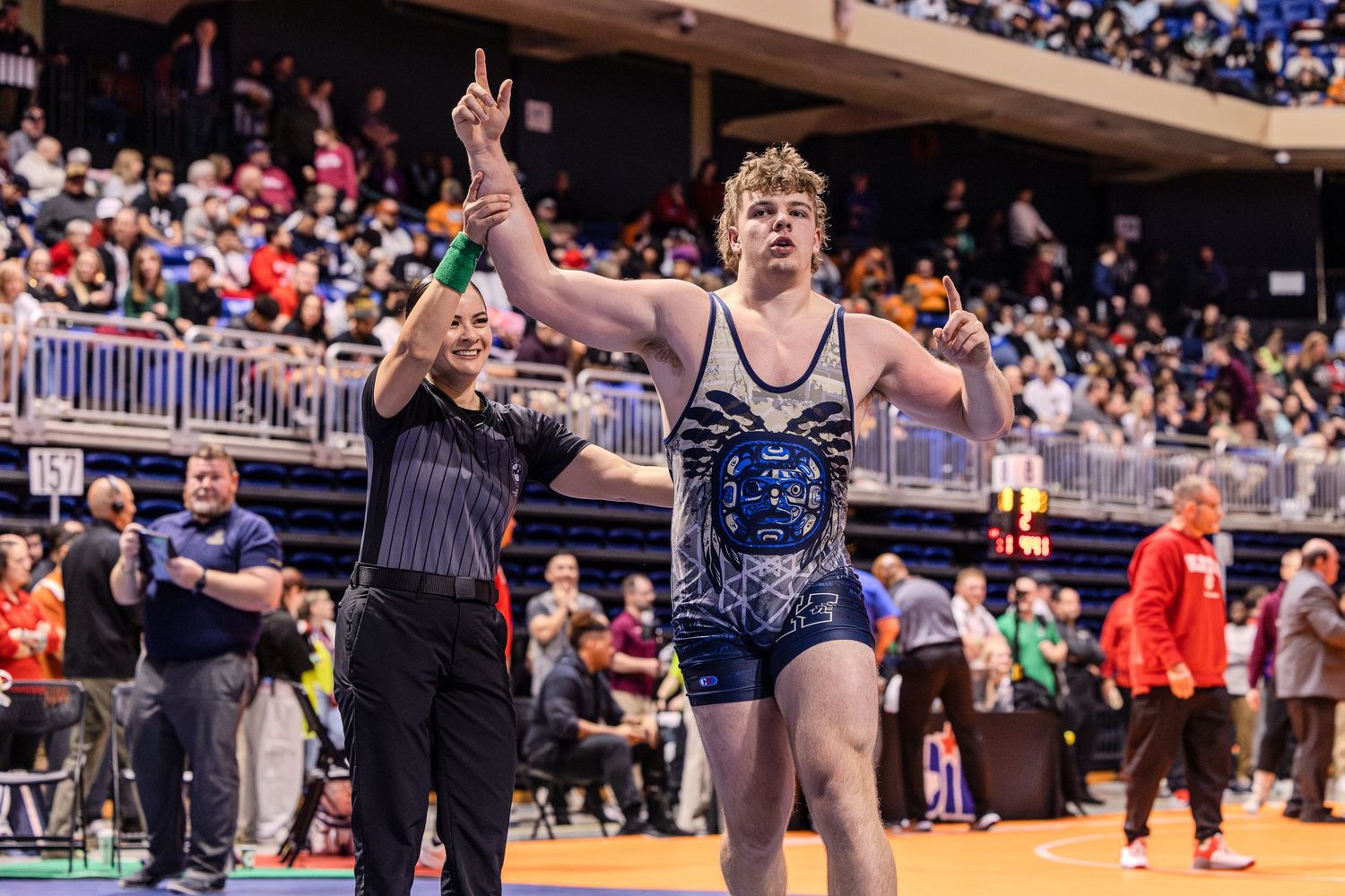 Wrestlers compete in a high school tournament with spectators watching from the bleachers in the background.