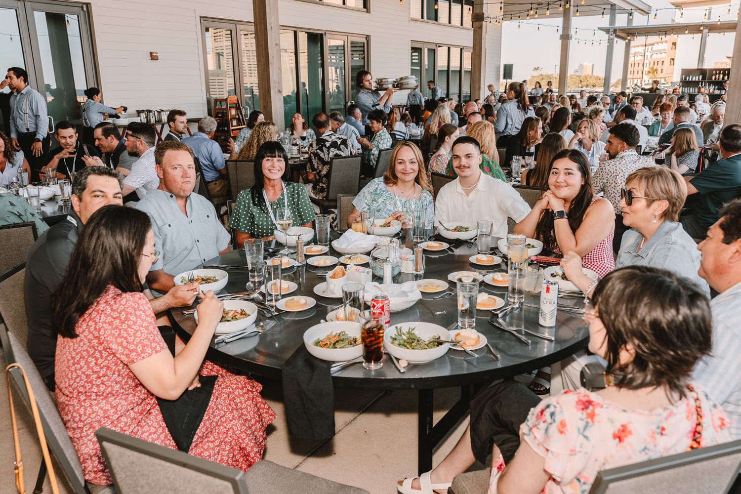 A group of people gathered around a round table at a large indoor event space enjoying a meal together.