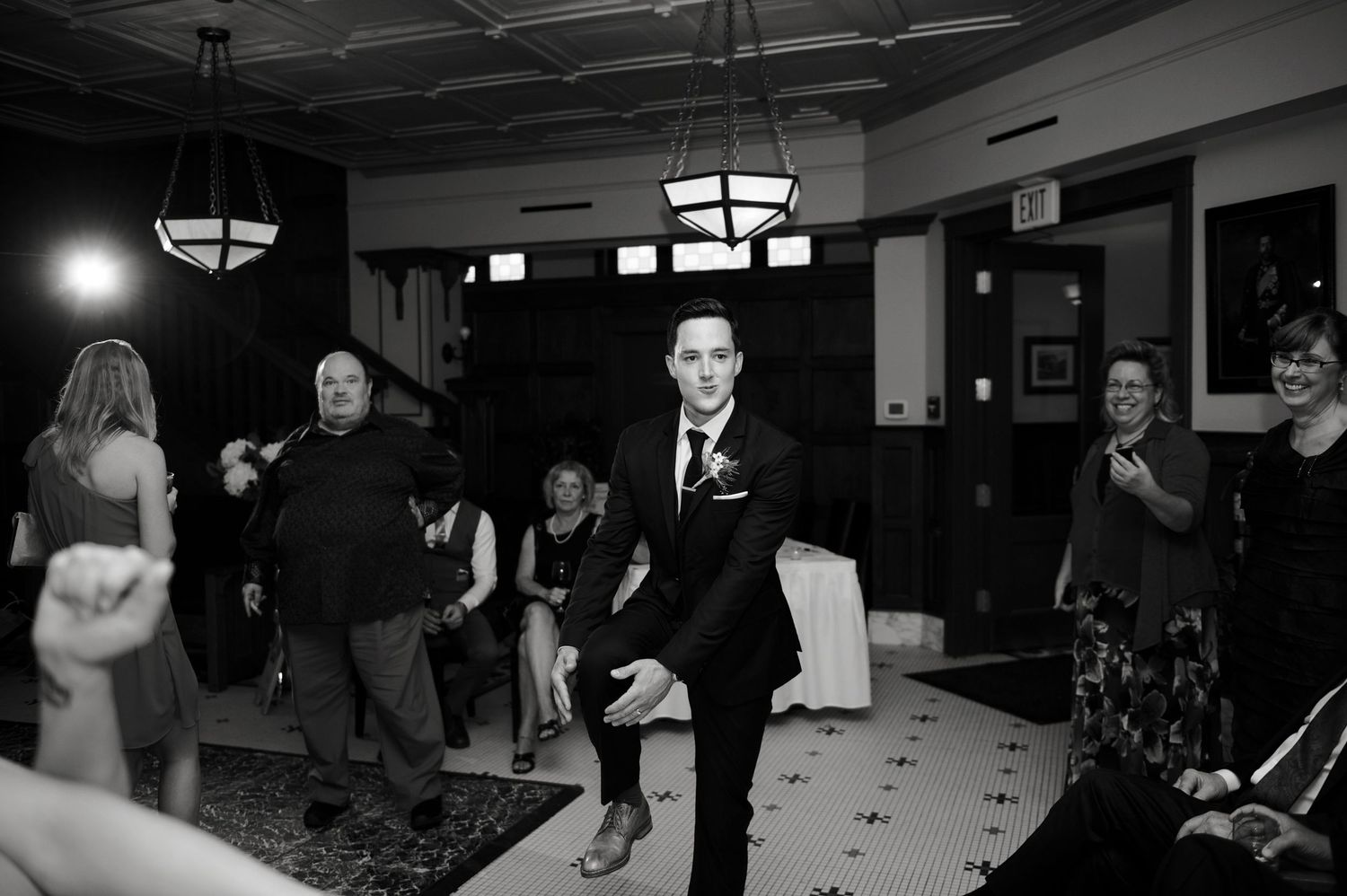 Black-and-white photo of a groom walking confidently through a cheering crowd on the dance floor.
